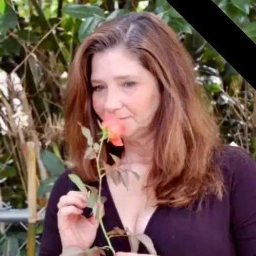 Woman smelling a rose in a garden with a black diagonal stripe in the top right corner.