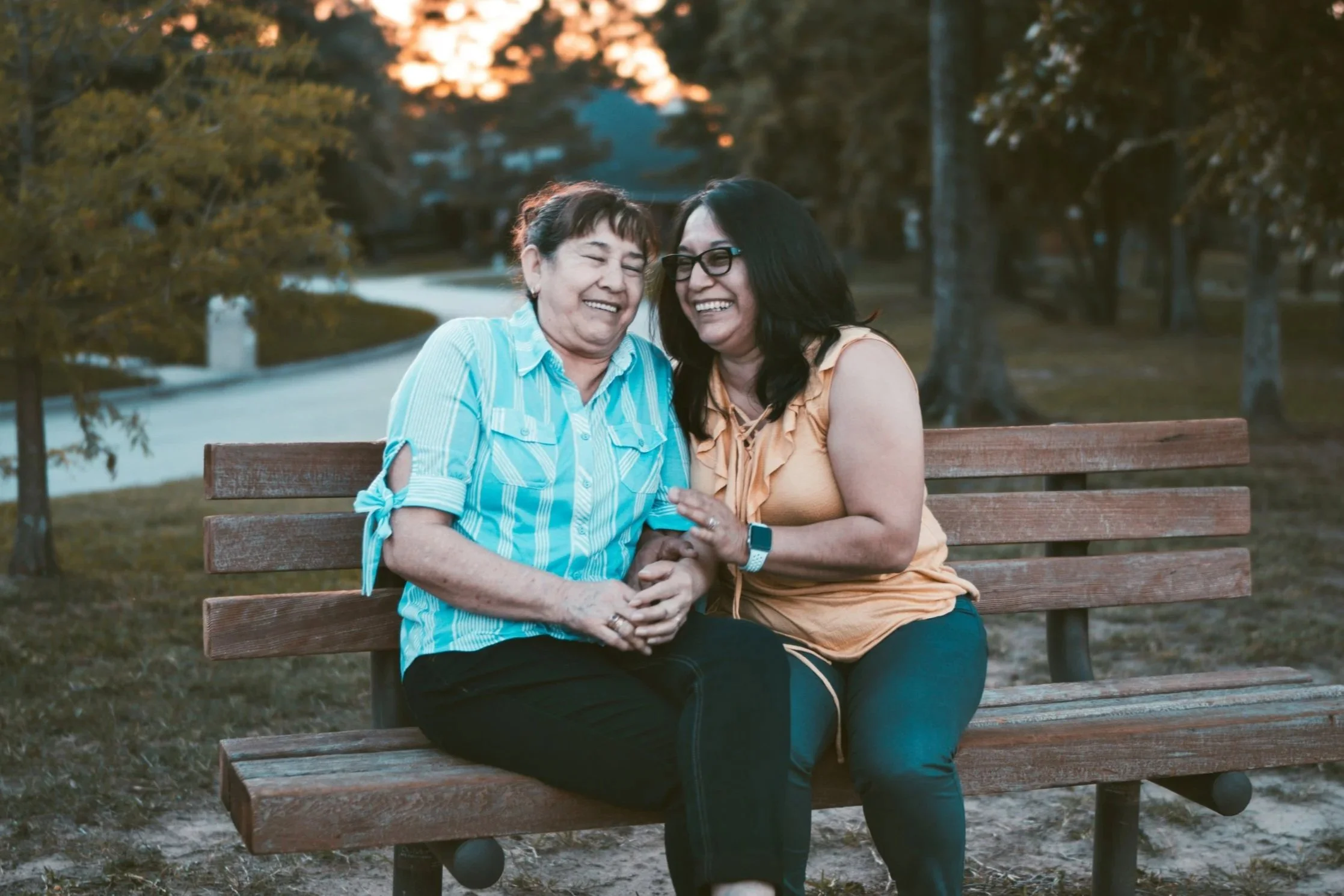 Two women sitting on a park bench, laughing and enjoying each other's company during sunset.