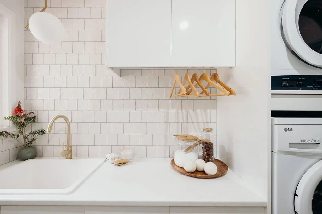 Laundry space with white cabinetry, brass tapware, timber hanging rail and simple styling in a Hill House renovation.
