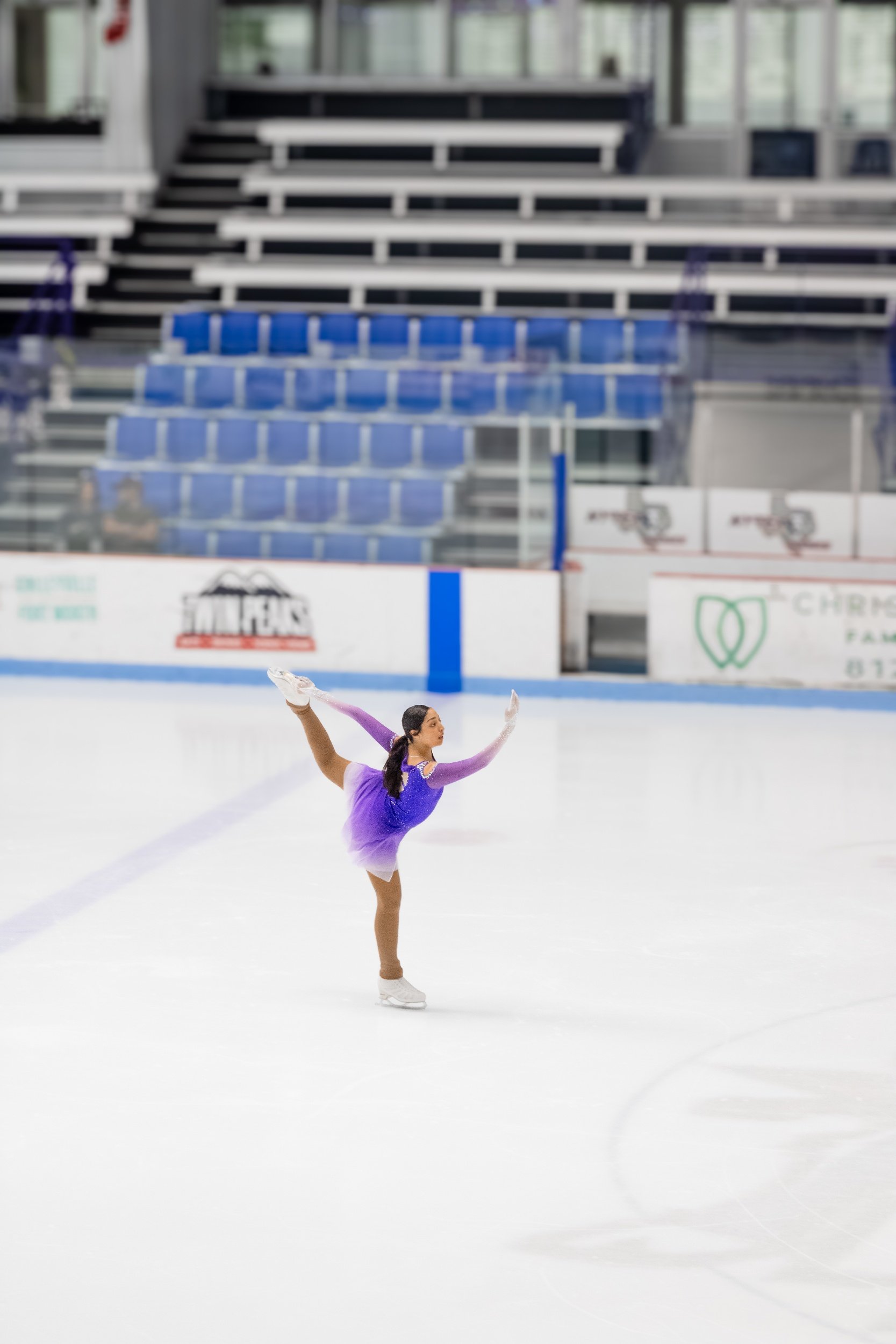A female figure skater in a purple costume performing a spin on an indoor ice rink.