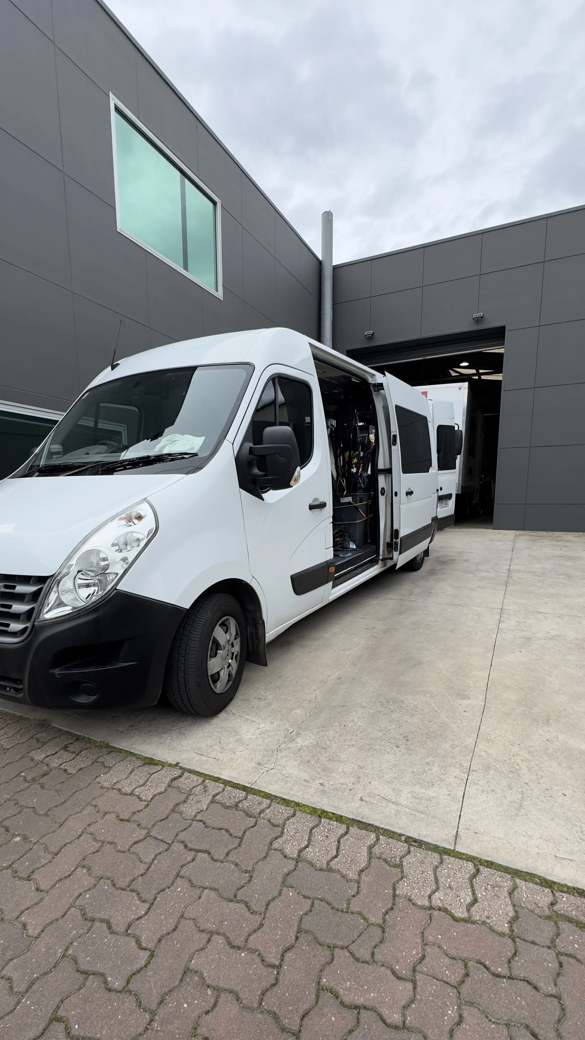 White van parked outside a garage with sliding door open, exposing tools and equipment inside.