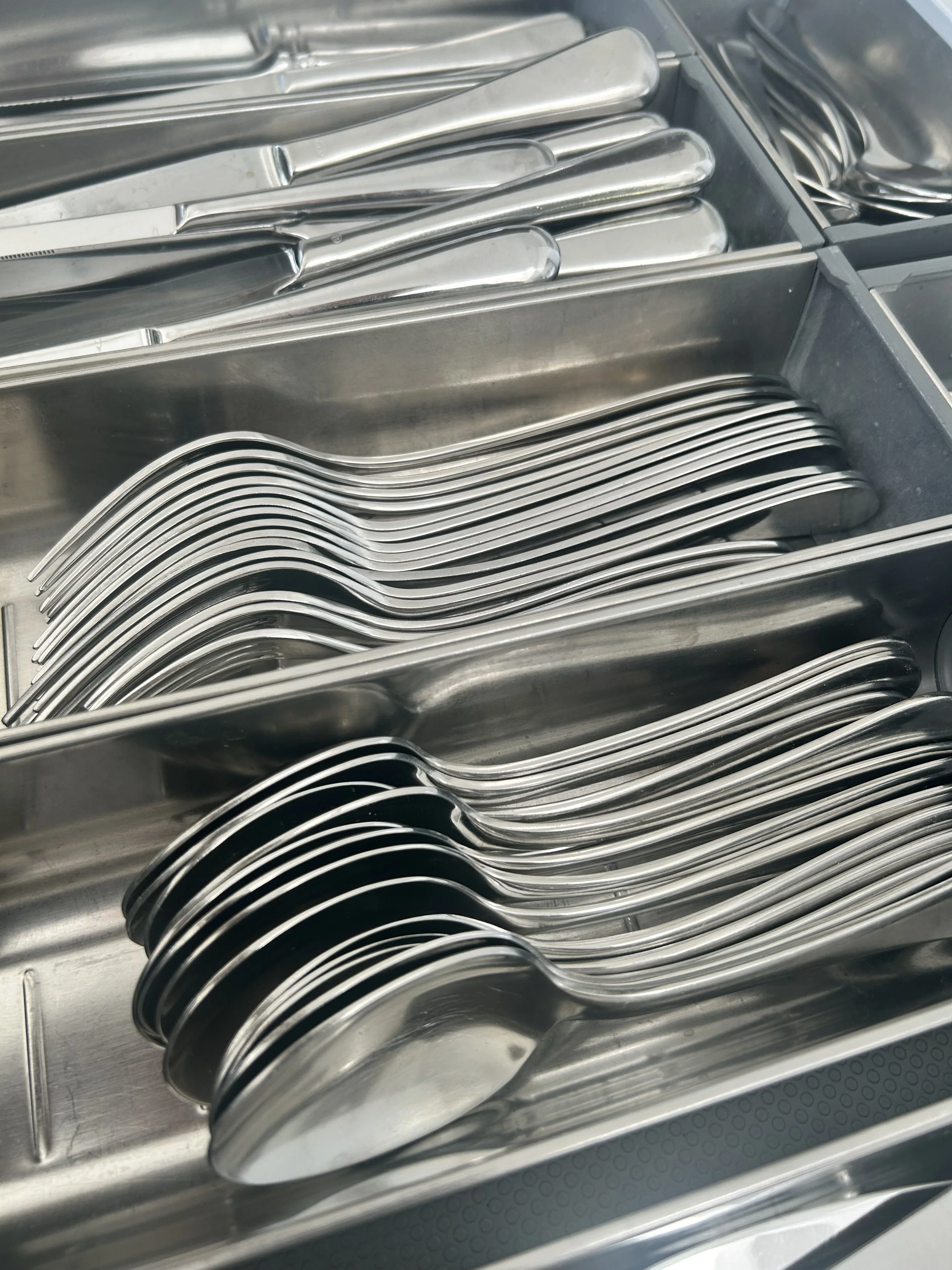 Drawer with neatly arranged stainless steel cutlery, including forks, knives, and spoons.