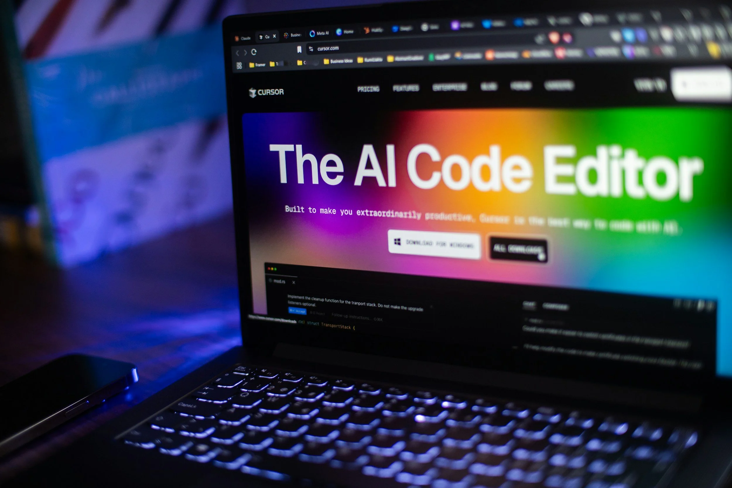 パソコンの画面に「The AI Code Editor」と書かれたウェブページが表示されている。背後には複数のブラウザタブが見える。