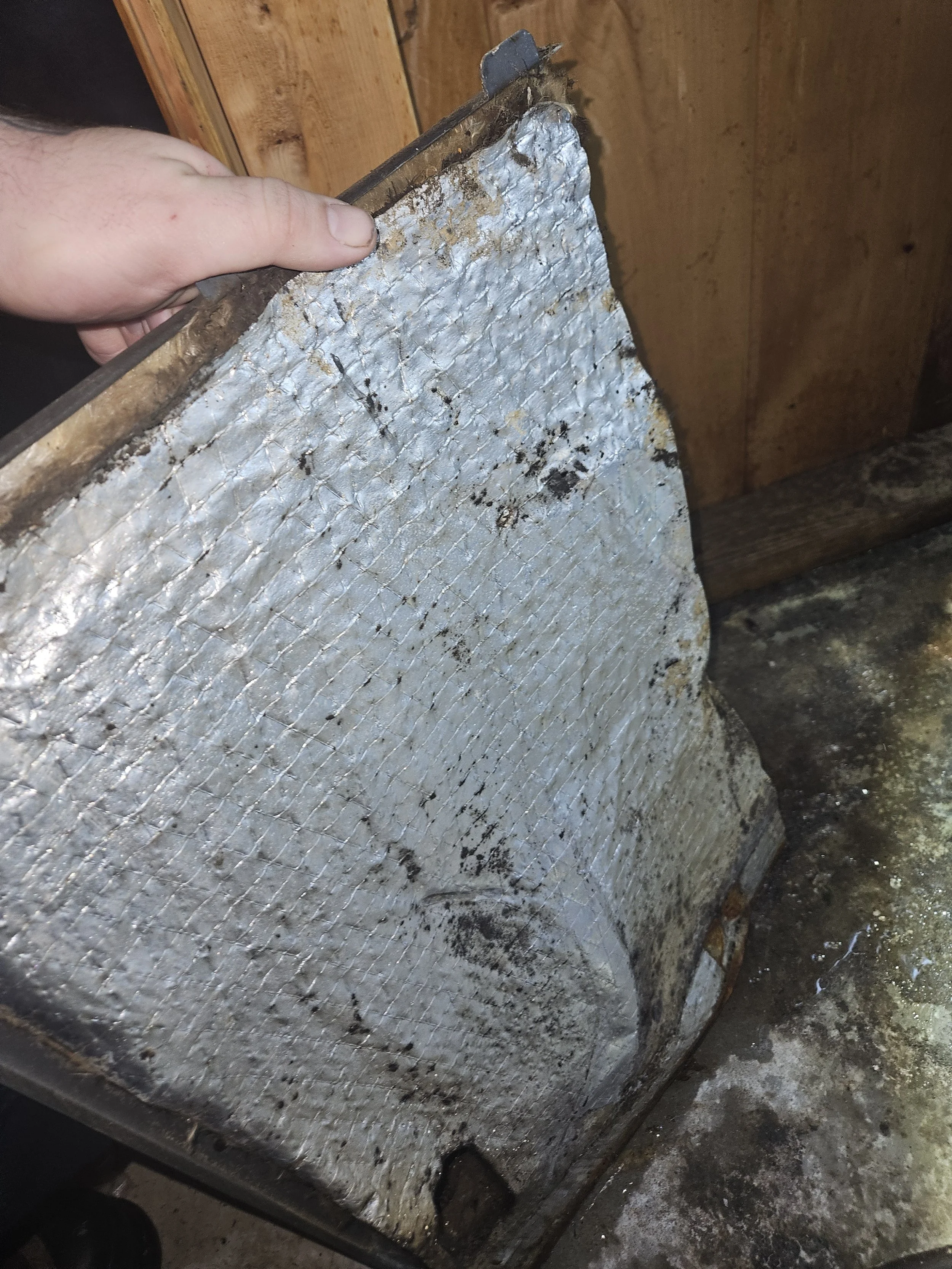 A person holding a dirty, used metal ice cream container with a wire cooling rack inside, in a rustic setting.