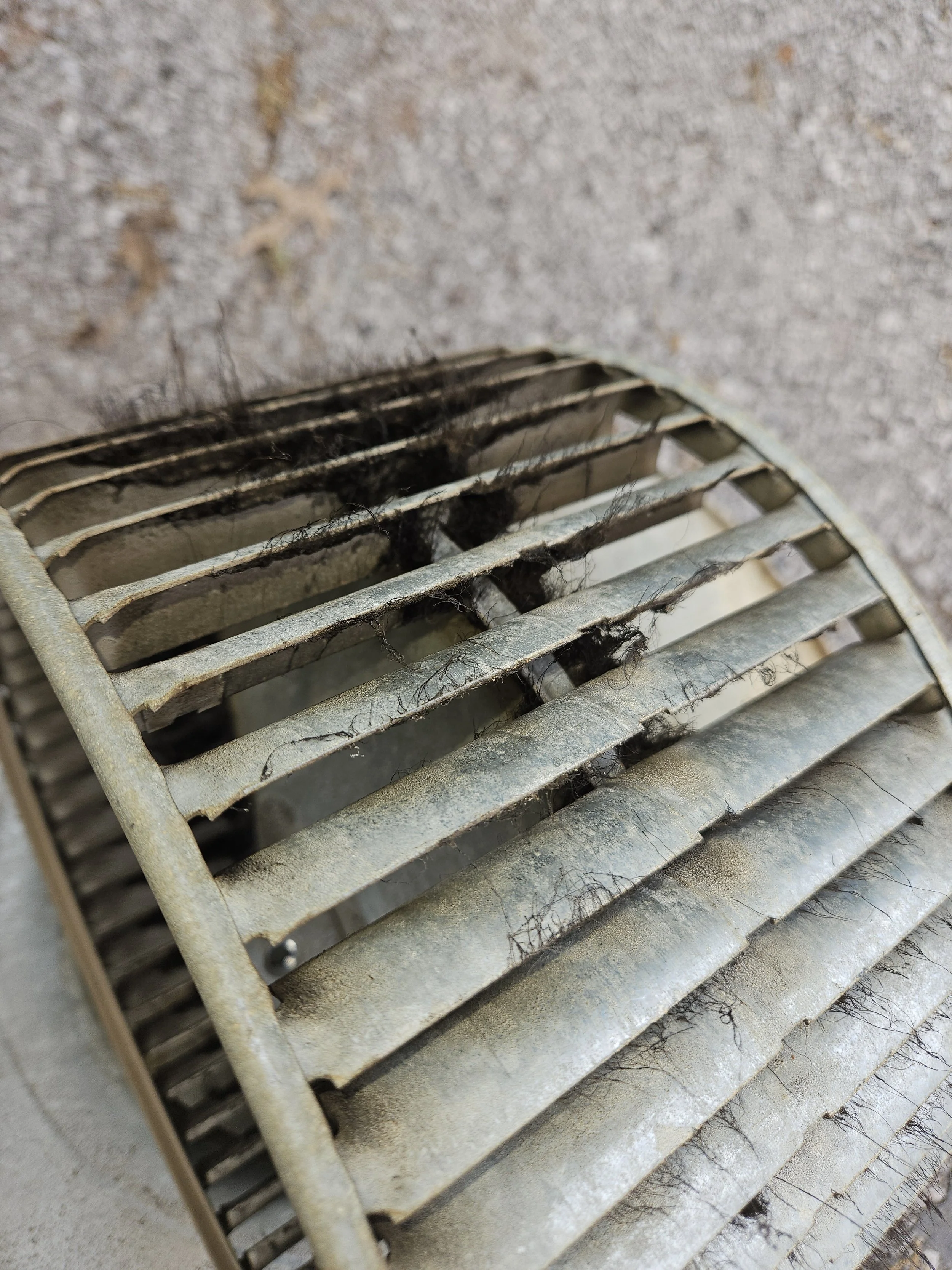 Dirty air vent with dust, pet hair, and debris on metallic slats.