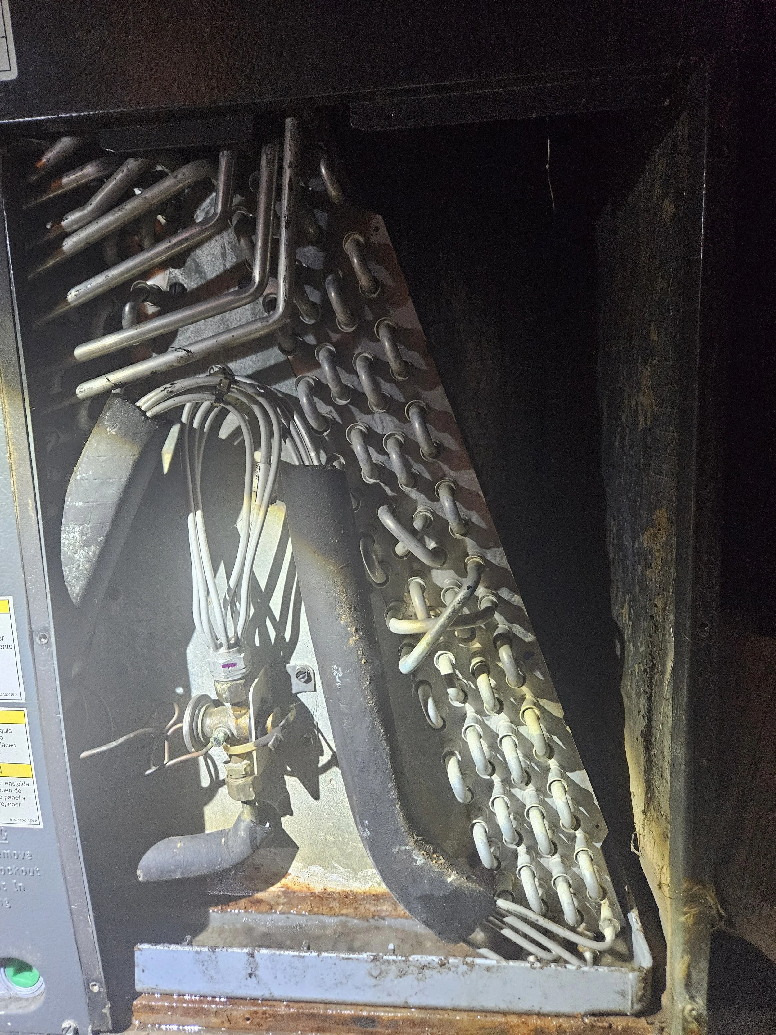 Interior view of an old, rusty industrial machine with metal pipes, wires, and a metal panel inside a dark metal casing.