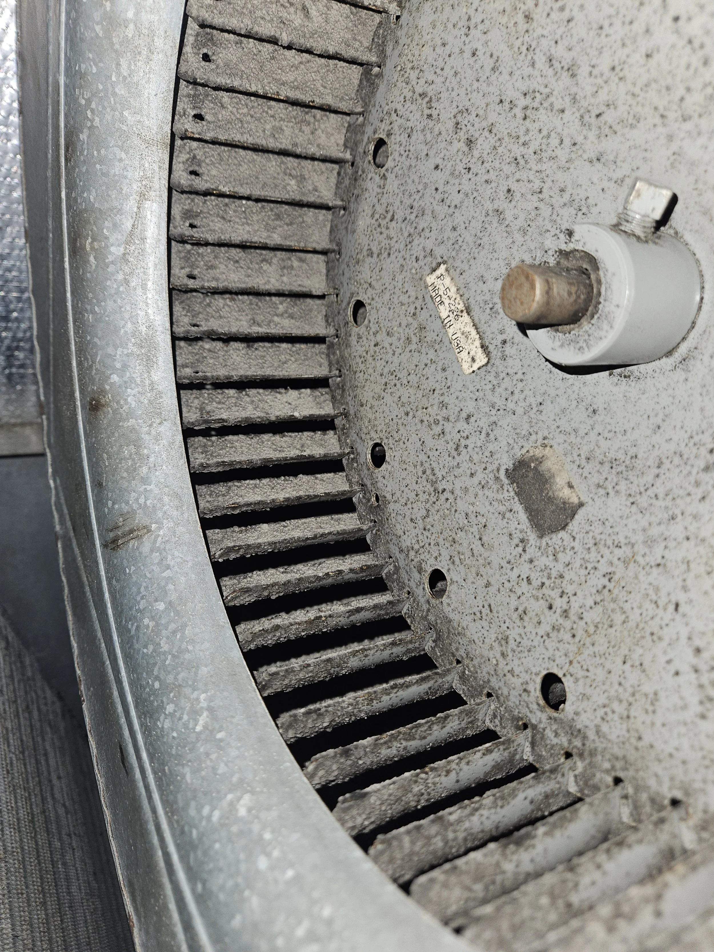Close-up of a dusty industrial turntable or motor component with a metallic casing, visible gear teeth, bolts, and a label.