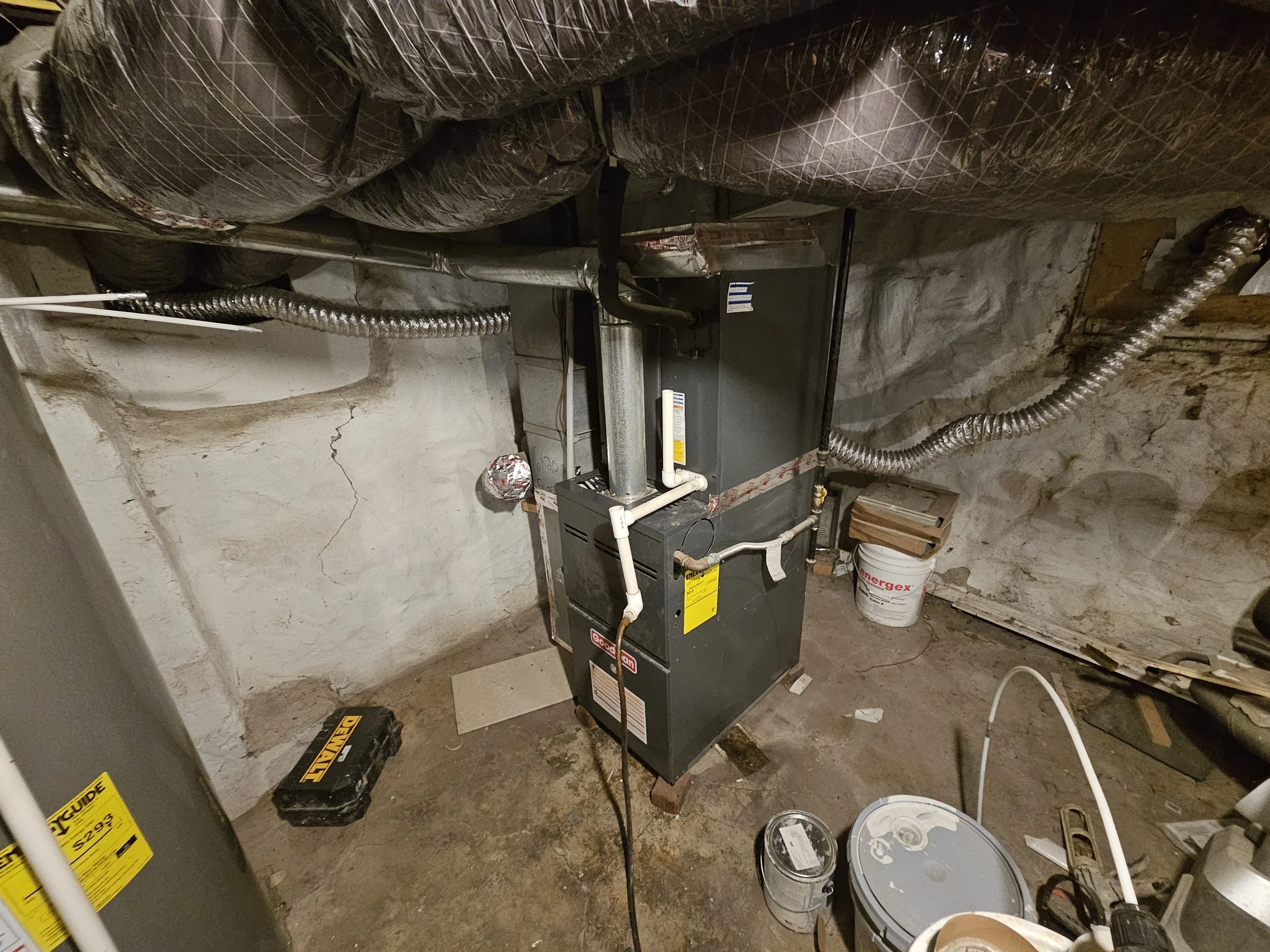 Basement utility room with a furnace, ductwork, and various tools and supplies scattered on the floor.