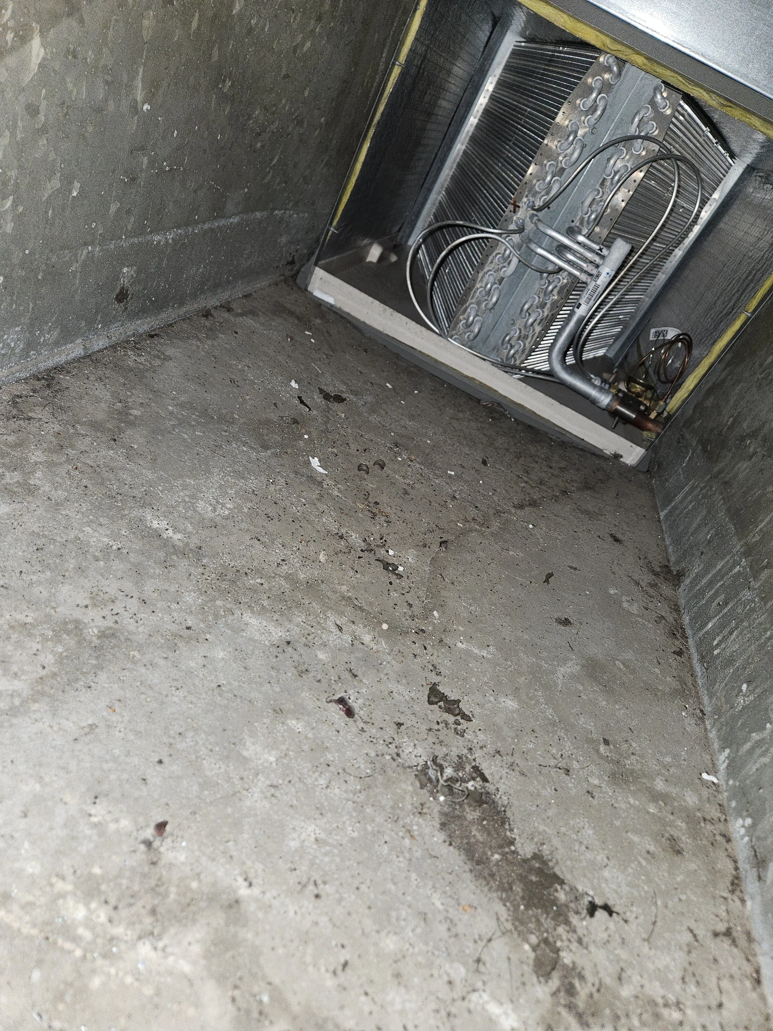 Empty concrete floor in a basement or utility room with an HVAC or refrigeration system installed in the corner.