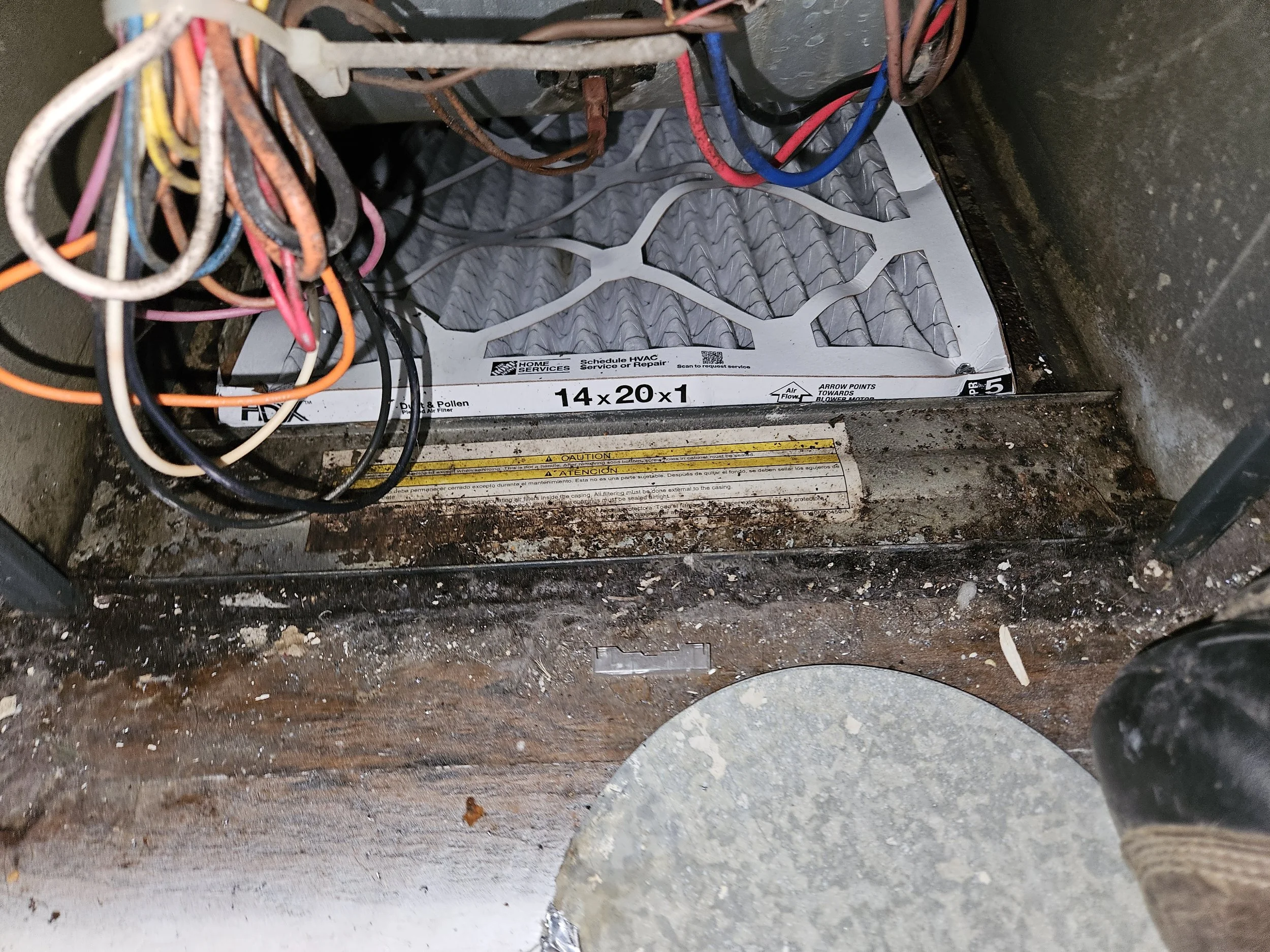 The interior of an HVAC unit or furnace with exposed wires and a dirty, dusty floor.