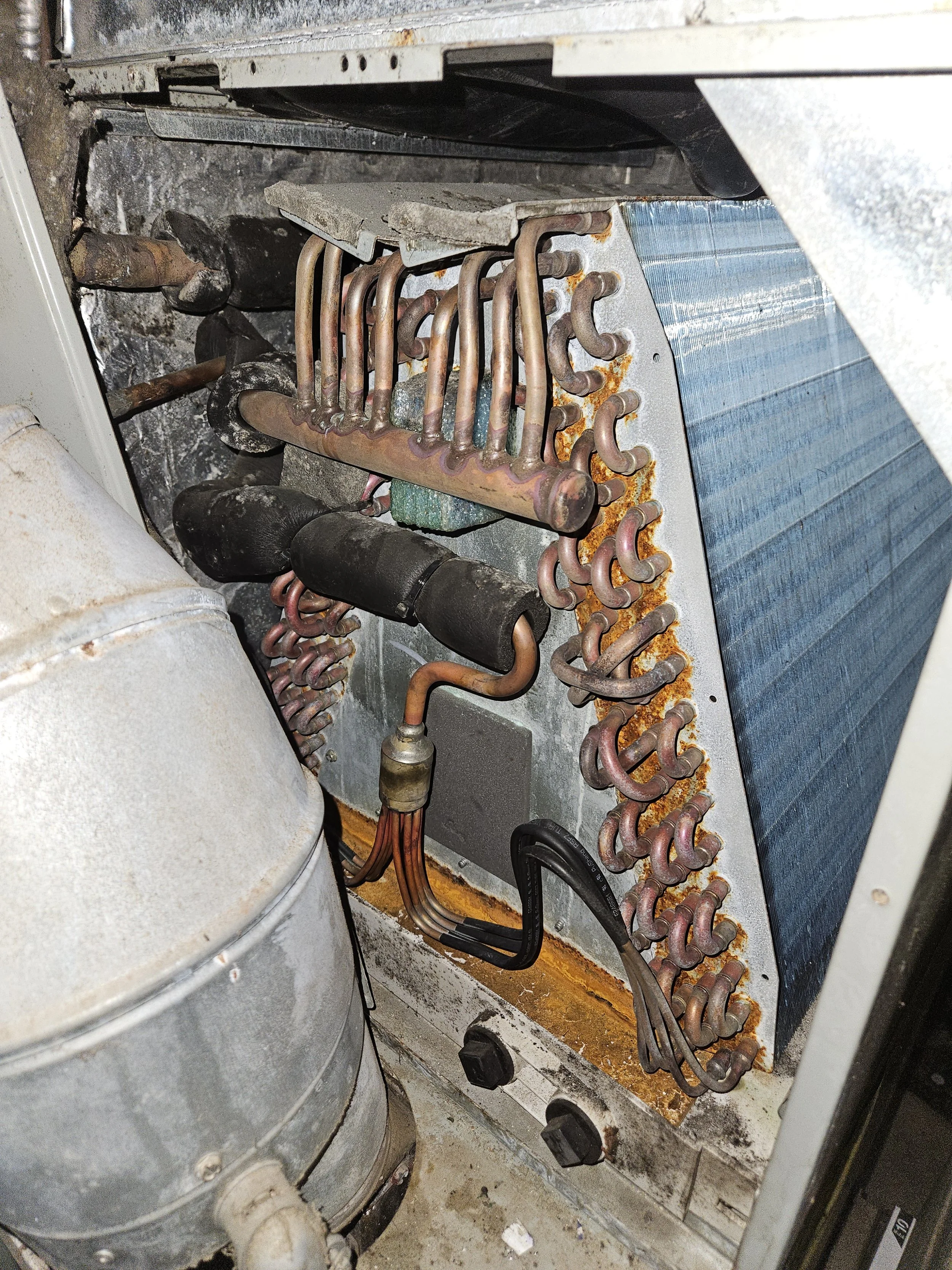 Interior view of an old air conditioning or refrigeration unit with rusted copper pipes, some insulation, and a large metal compressor.