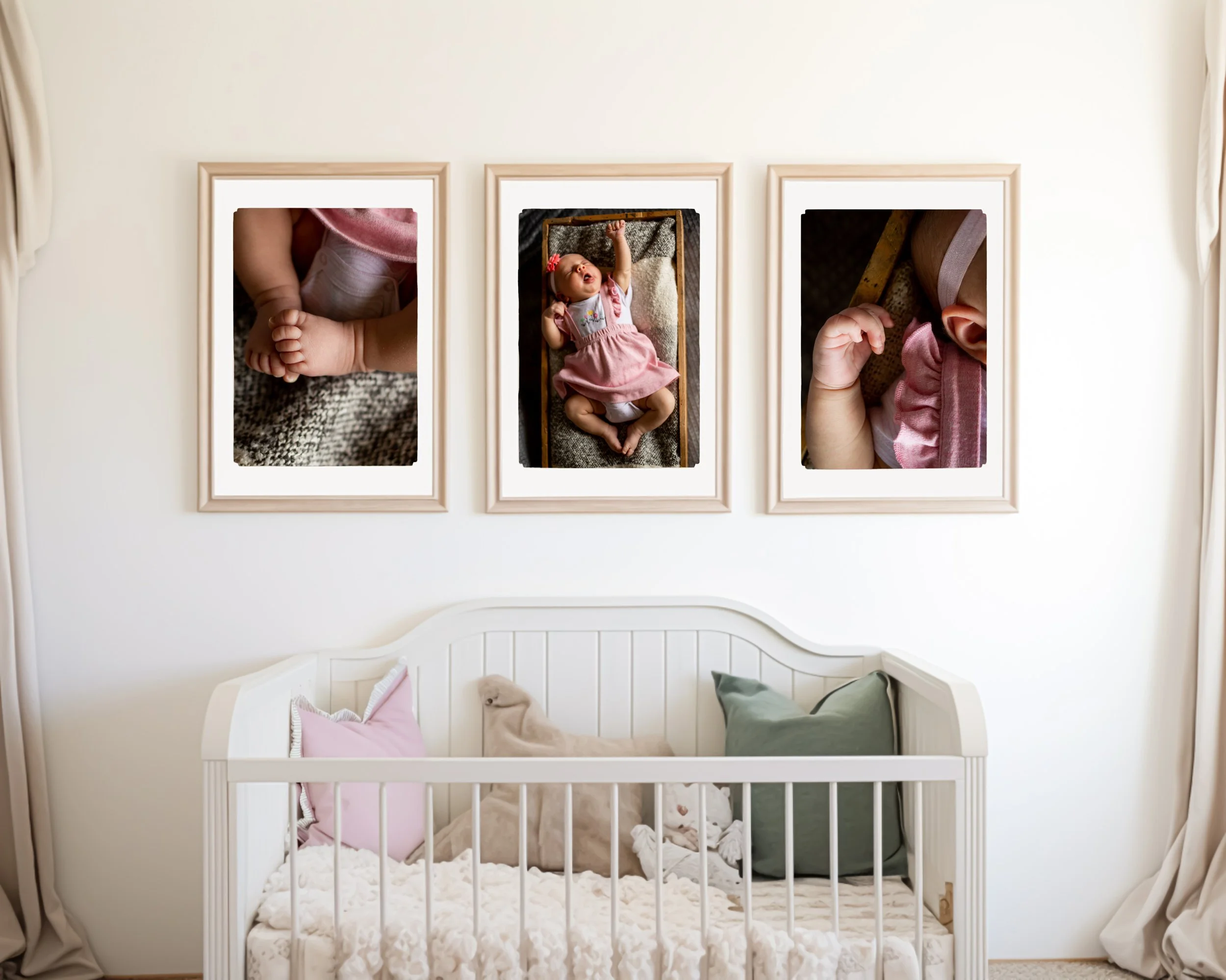 Three framed photos of a baby girl are hung above a white crib with pink and green pillows and stuffed animals inside. The photos show close-ups of the baby's hands, face, and arm.