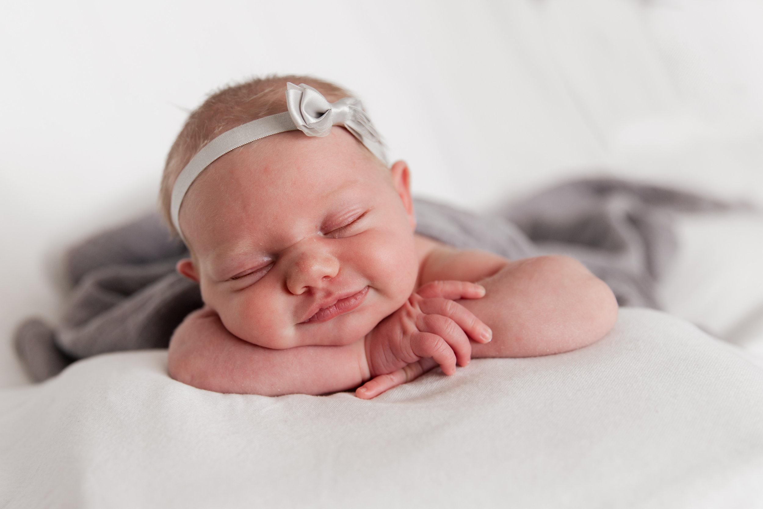 A sleeping newborn baby with a white headband and gray clothing resting on a white surface.