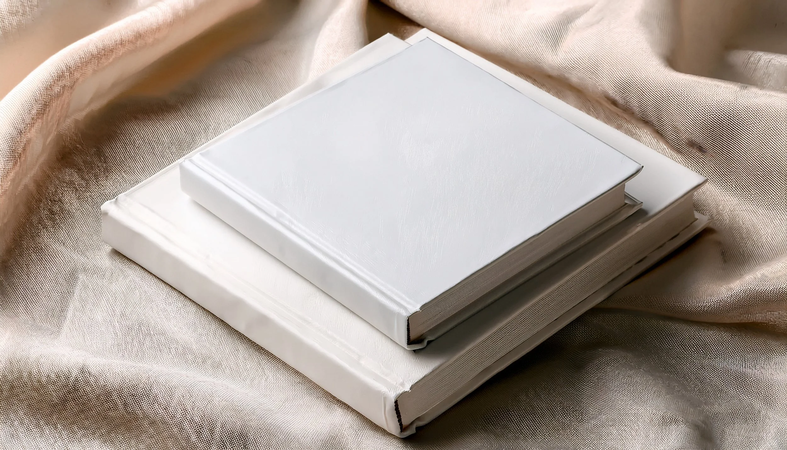 Two white hardcover photo albums stacked on beige satin fabric.
