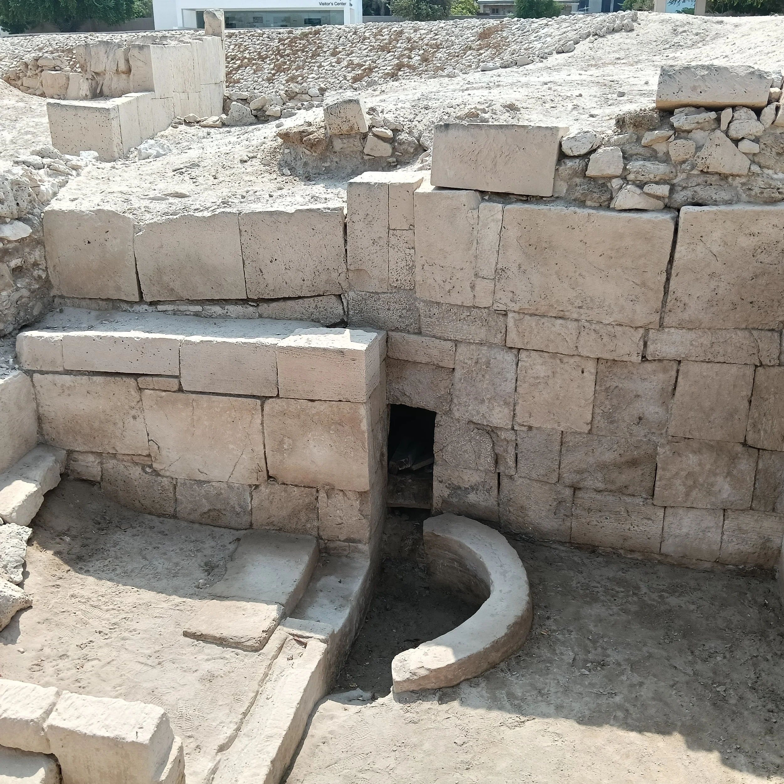 Large squared stone blocks frame a small dark opening above a curved stone basin-like feature, with steps at the left.