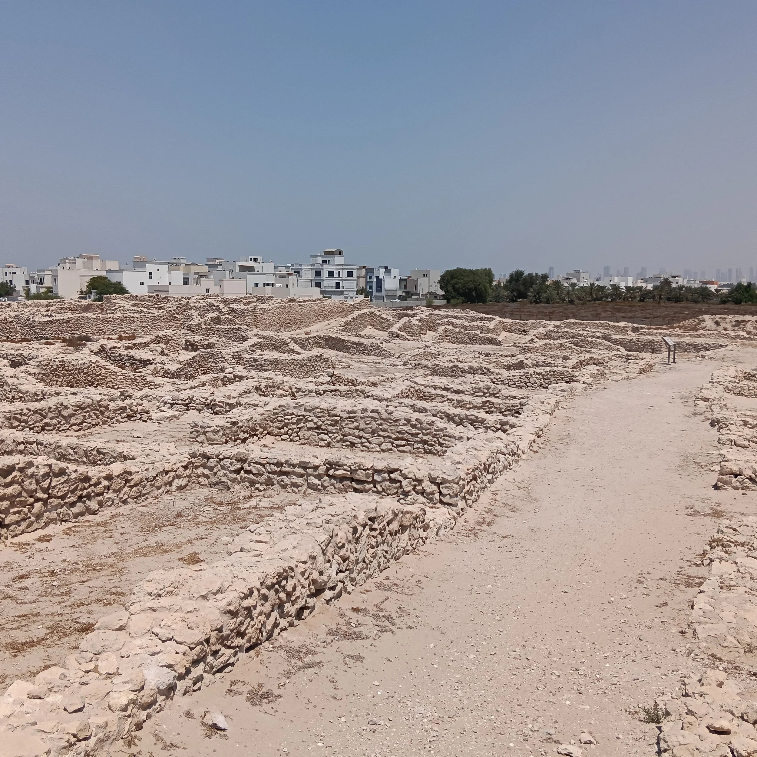 A broad sandy passage extends between low stone walls towards modern white houses.