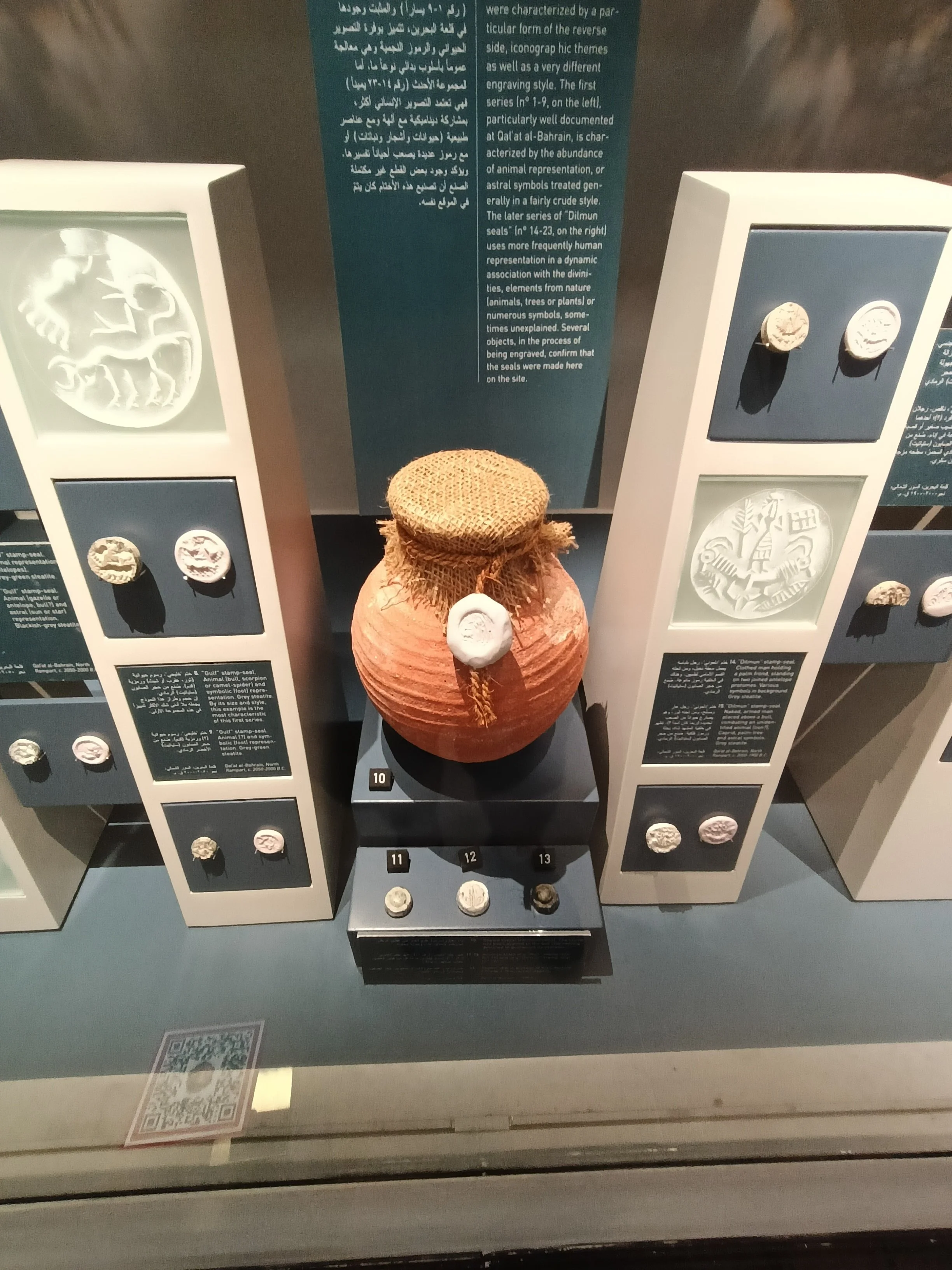 Small circular seals and enlarged impressions surround a reddish pot with a fabric-covered neck and a seal attached to a cord.