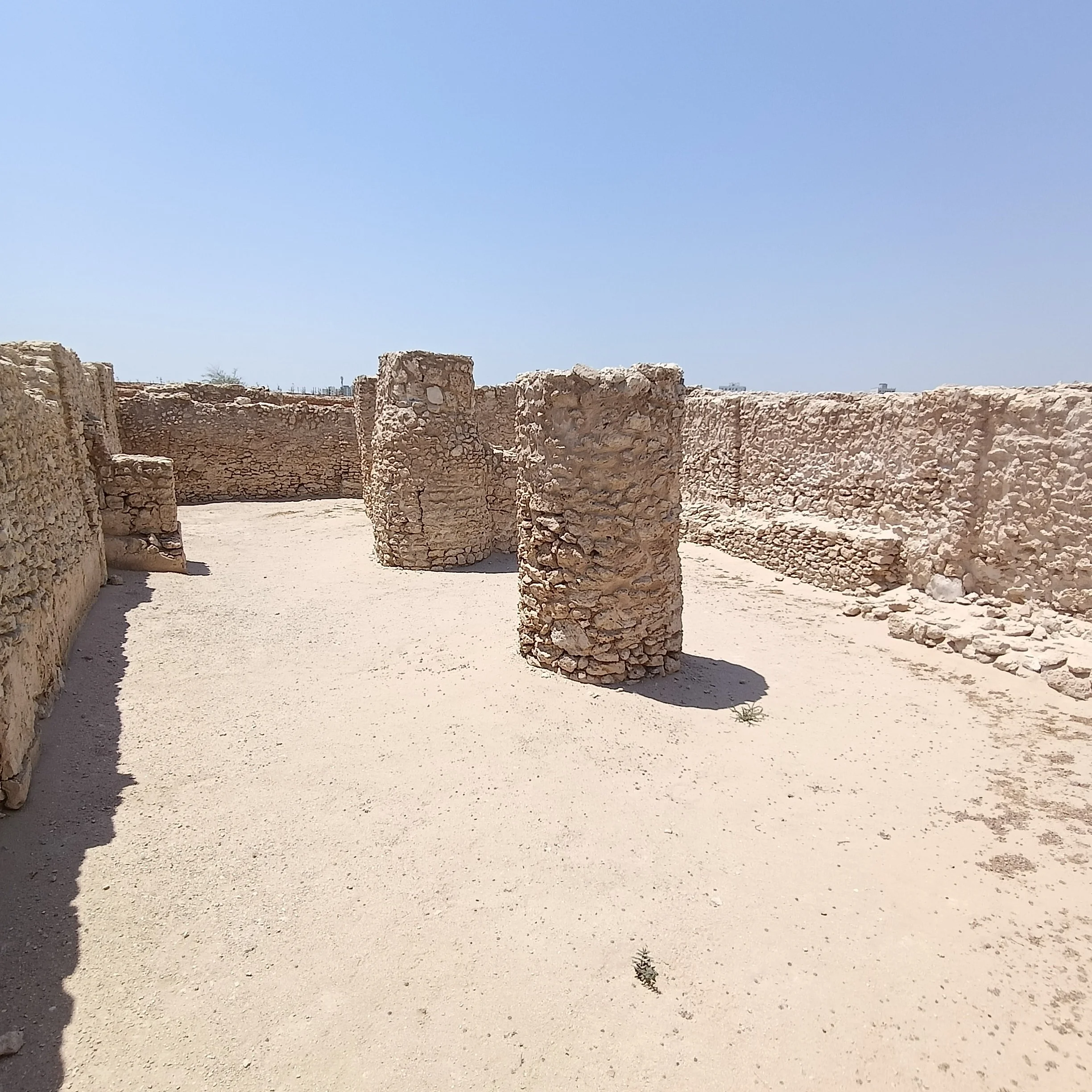Two substantial rounded stone pillars stand inside a roofless room enclosed by rough-stone walls.