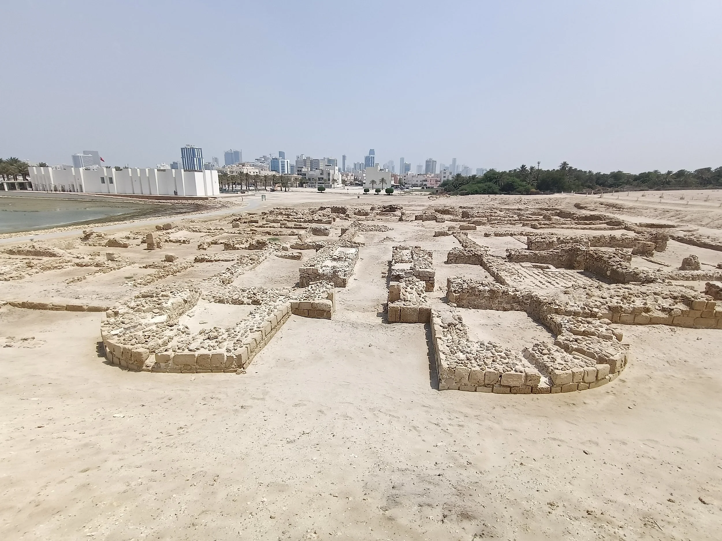 A central open passage runs between low masonry with rounded ends, towards a dense grid of spaces and the modern skyline.
