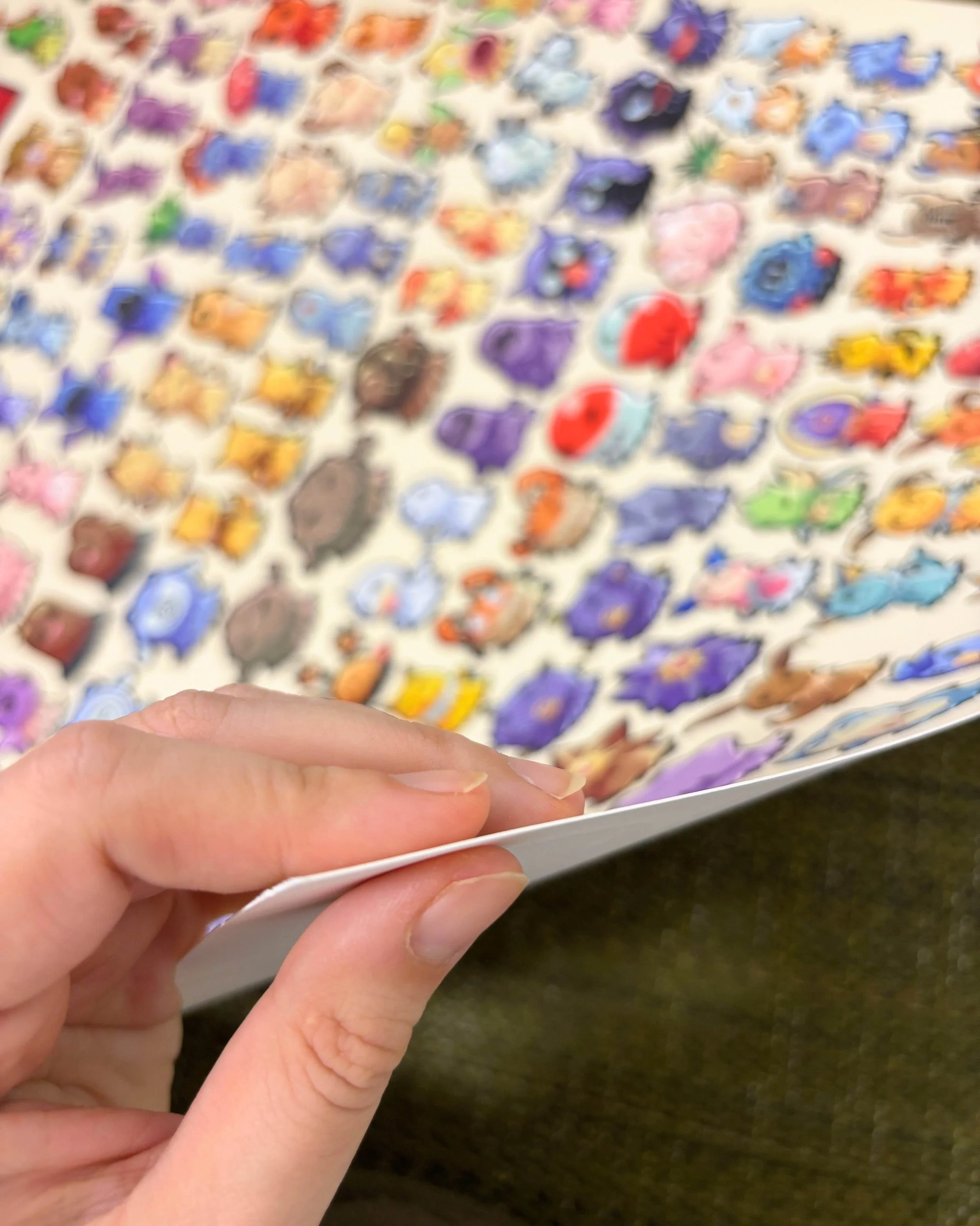 Hand holding a fine art print with various colorful cartoon animal characters on it. Mimikyu Pokémon Kanto region. mori.ink