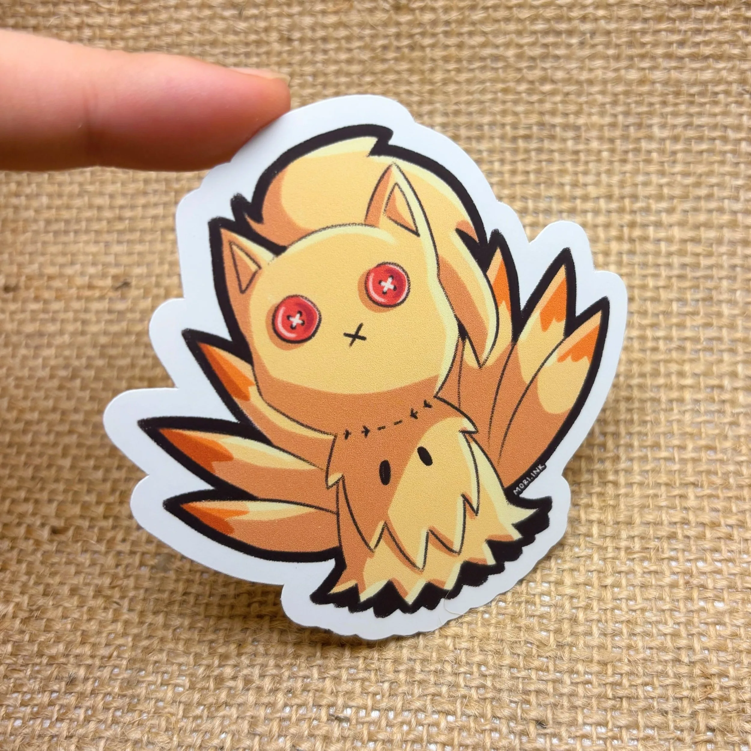 Ninetales Pokémon sticker. A cartoon sticker of Flareon as a cute plush with red eyes, sitting against a textured fabric background. Mimikyu Pokémon Kanto region. mori.ink