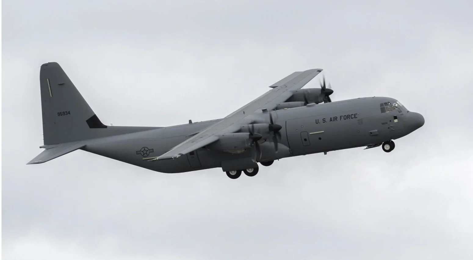 A U.S. Air Force cargo aircraft flying in the sky with a gray exterior and four propeller engines.