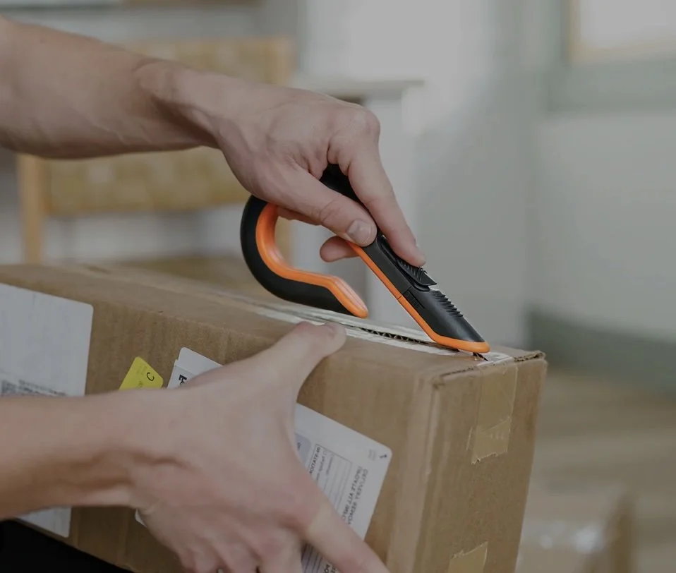 Person using a utility knife to open or cut into a cardboard box.