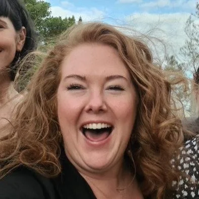 A woman with curly red hair smiling outdoors.