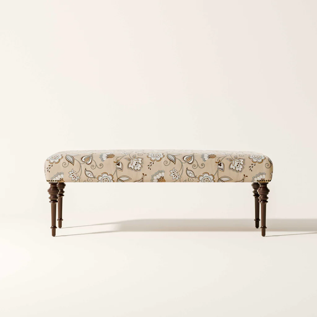 A floral-patterned upholstered bench with dark wooden legs against a plain white background.