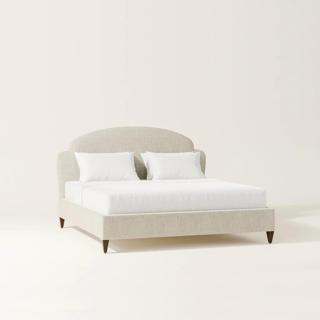 A beige upholstered bed with white bedding and two white pillows on a plain light-colored background.