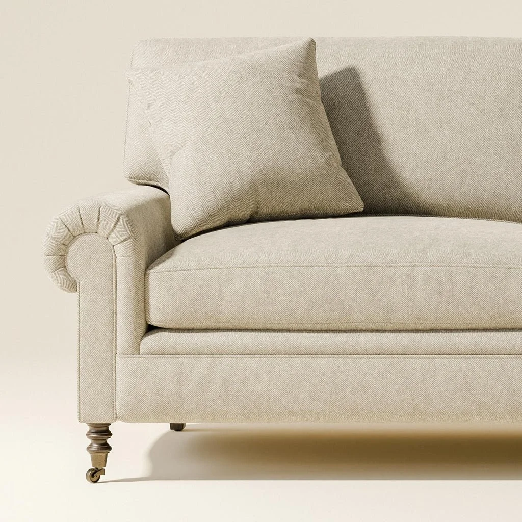 Close-up of a beige upholstered sofa with rolled armrest, cushion, and wooden legs with wheels.