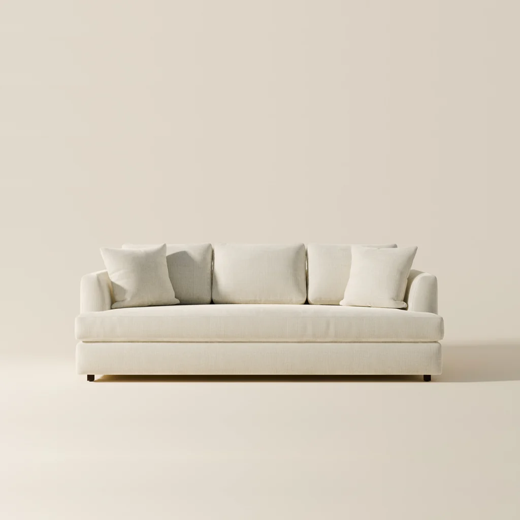 A white sofa with three white cushions is placed against a plain, off-white wall.