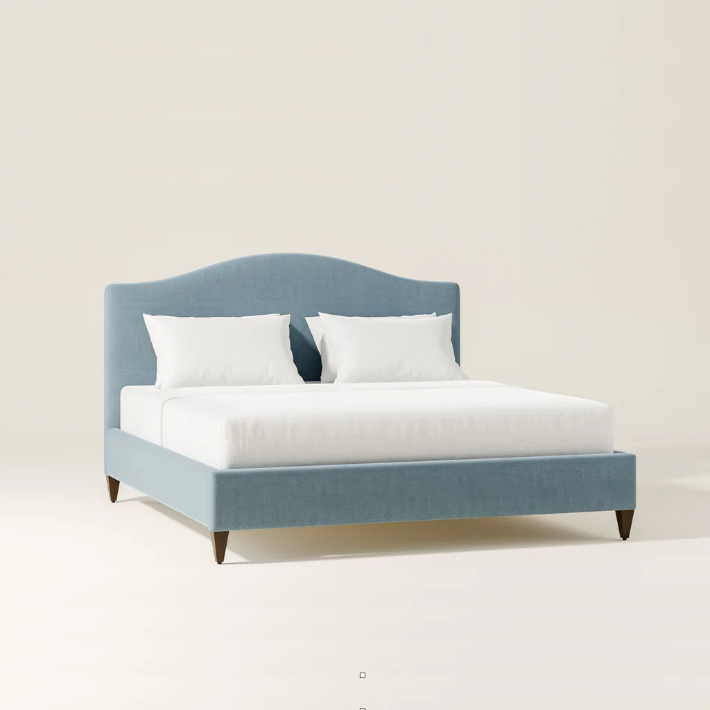 Blue upholstered bed with white bedding and pillows, against a plain beige background.