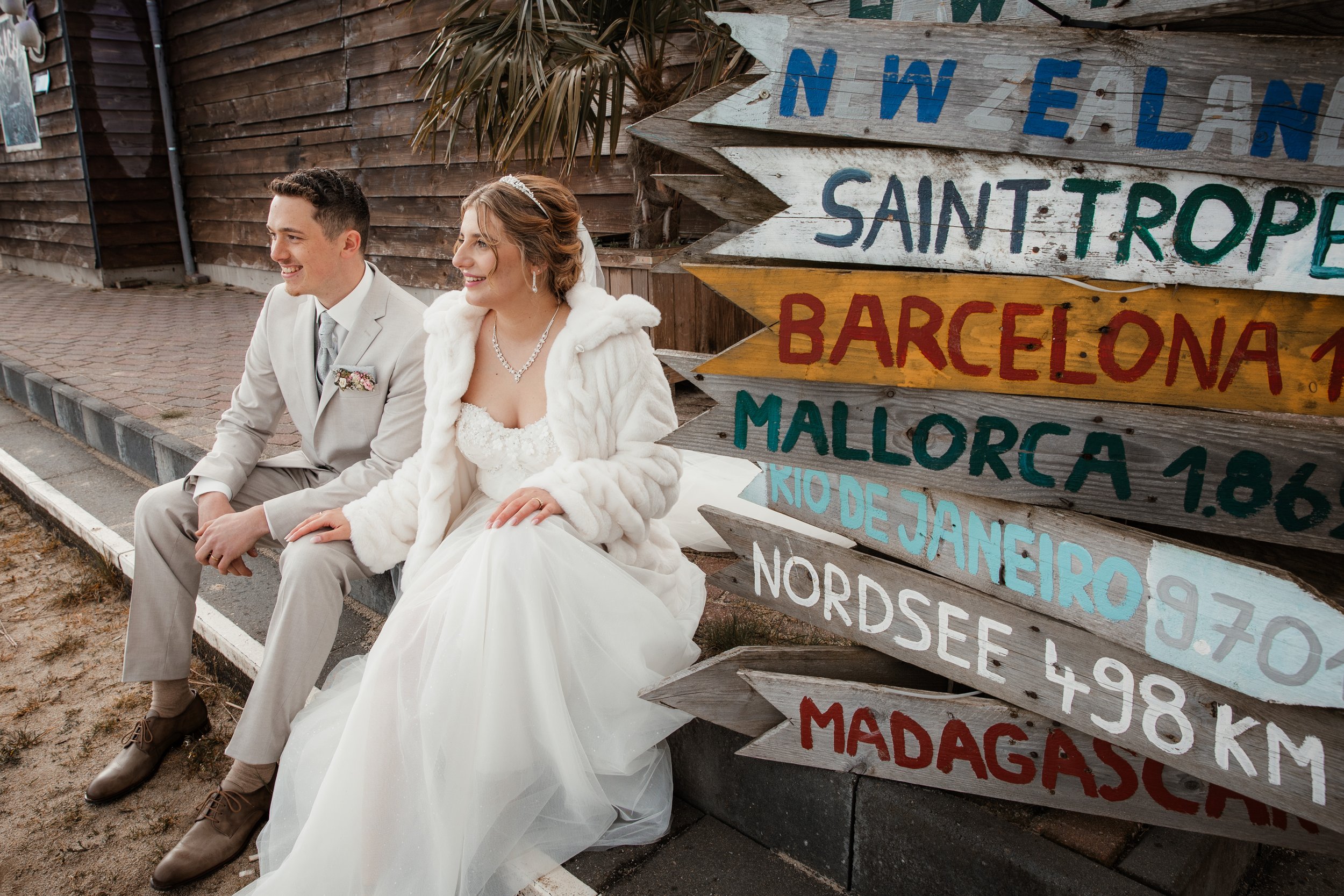 Brautpaar sitzt nebeneinander neben einem Wegweiser bei einem Hochzeitsshooting