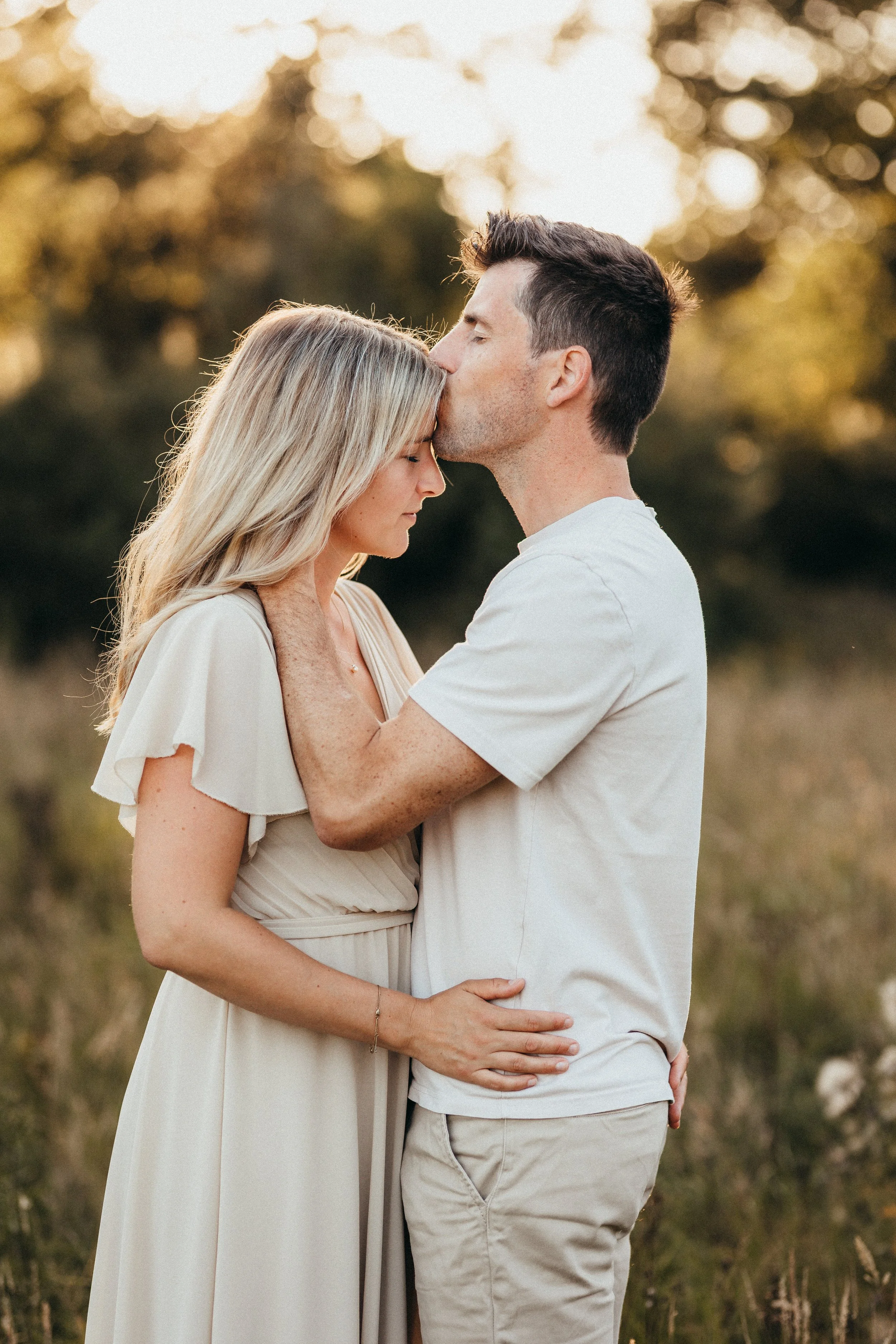 Paar küsst sich auf einer Wiese stehend bei Sonnenuntergang