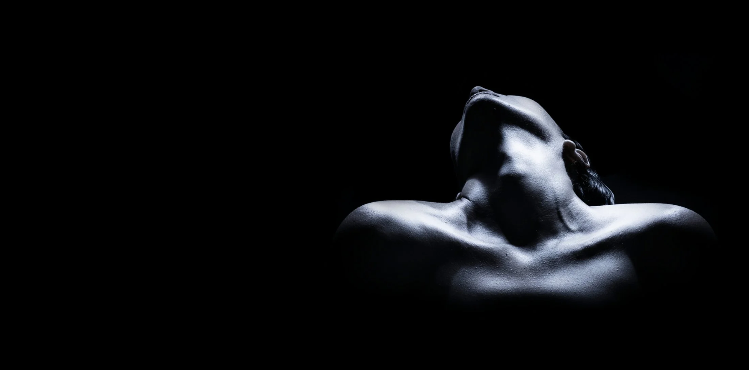 A black and white image of a woman with her head tilted back in ecstasy, illuminated by dramatic light highlighting her facial features and shoulders against a dark background.