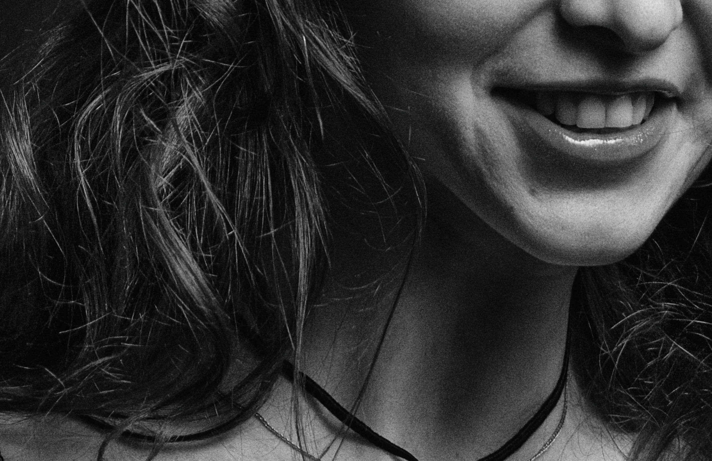 Close-up of a woman smiling, with curly hair and wearing necklaces, in black and white.