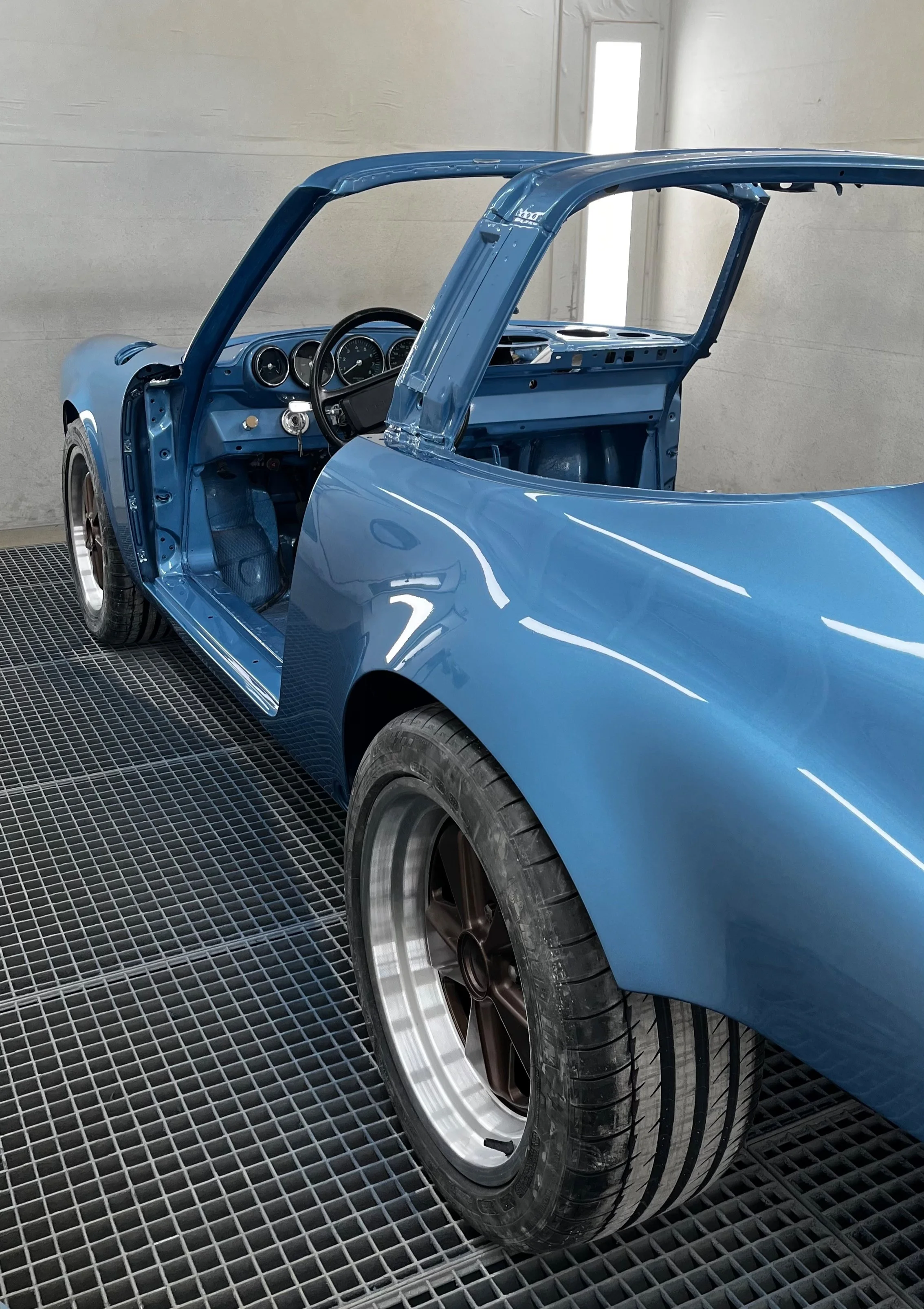Voiture en cours de restauration sans toit, avec peinture bleue et roues en métal.