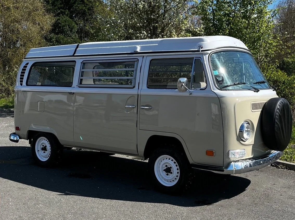 Un van vintage beige avec une roue de secours attachée à l'avant, stations sur une route près de la nature.