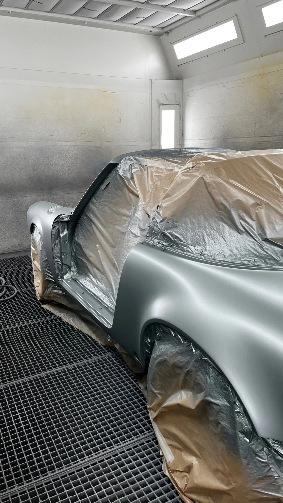 Voiture en cours de peinture dans un atelier, partiellement masquée par des feuilles de protection.