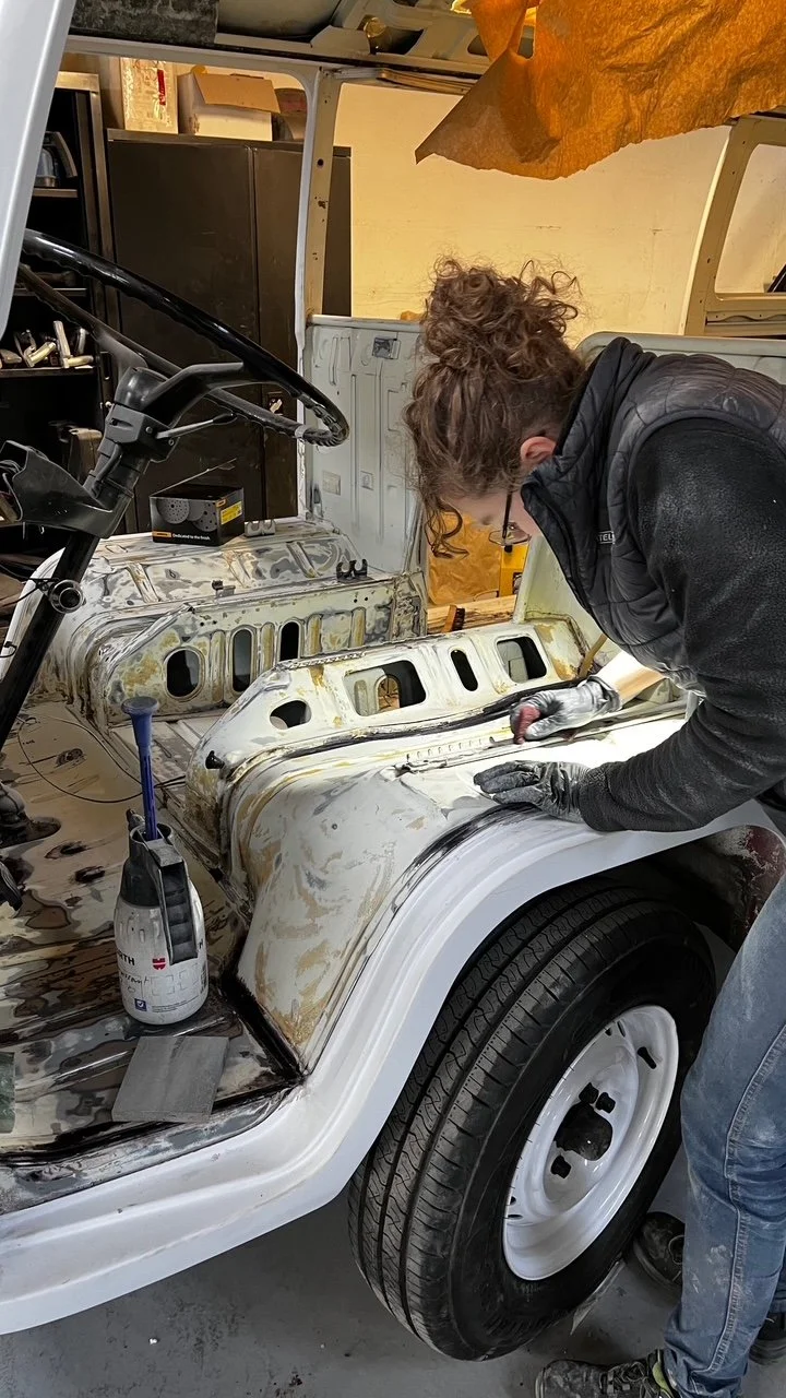Une personne faisant des travaux de carrosserie sur un véhicule ancien, apparence rouillée et en cours de restauration.