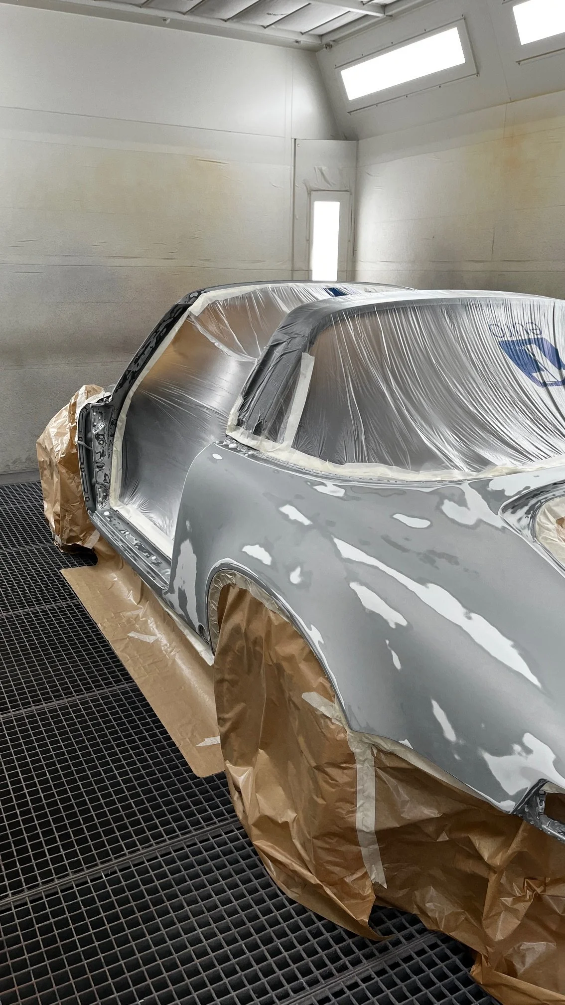 Voiture en cours de peinture dans un atelier, couverte de film plastique et de papier de protection.