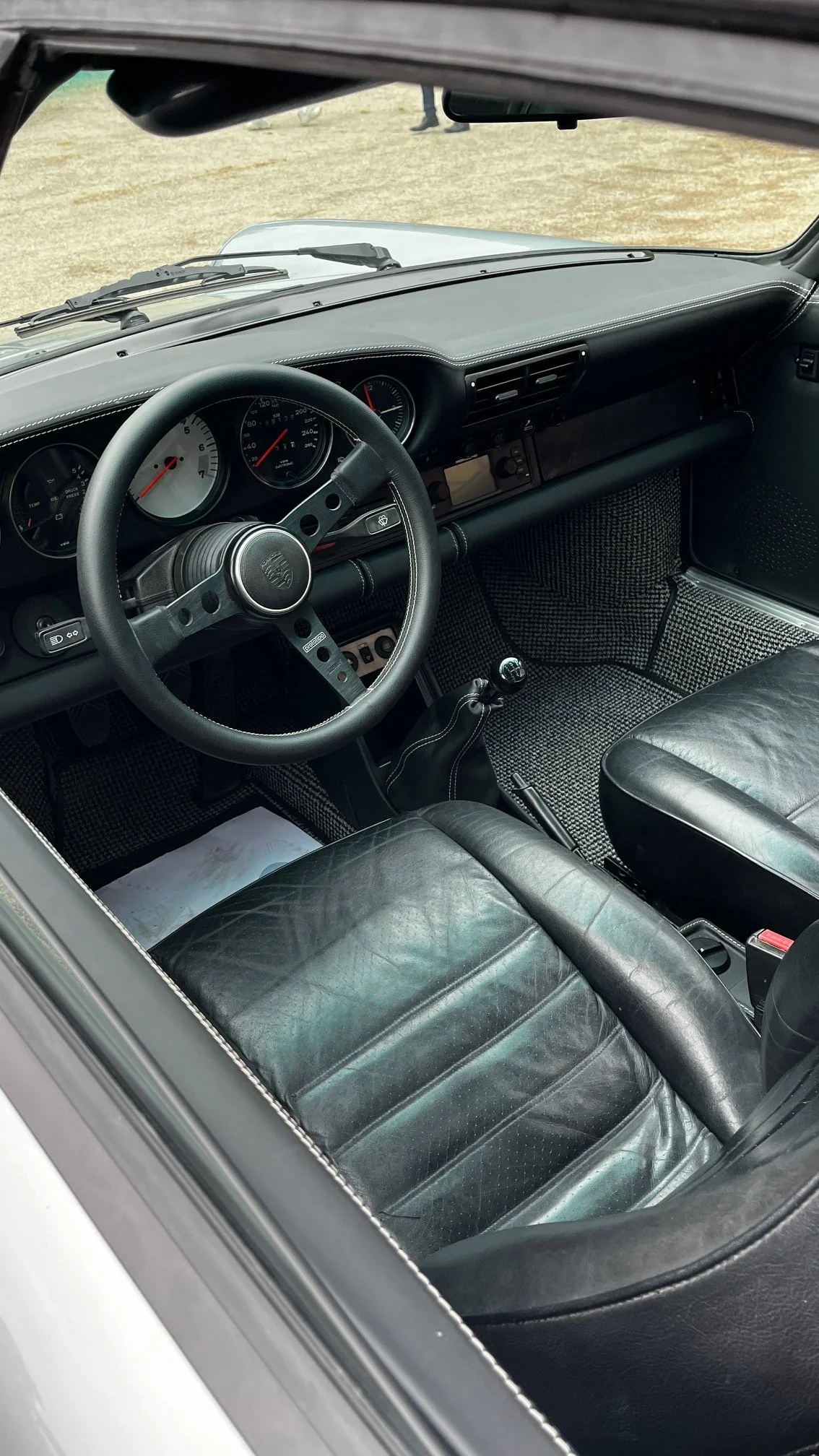 Intérieur d'une voiture classique, montrant le tableau de bord, le volant et les sièges en cuir noir.