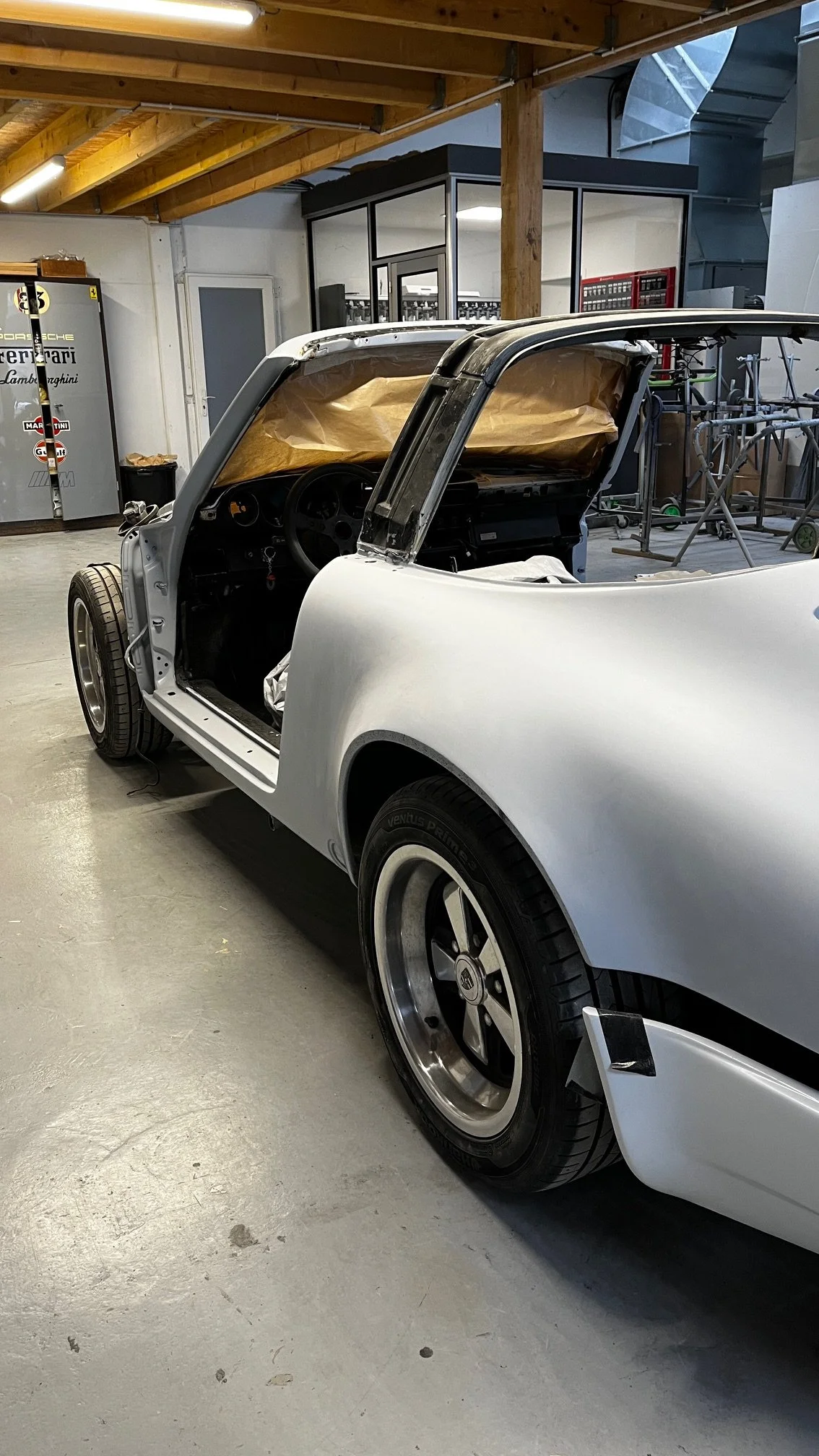 Voiture de course en restauration dans un atelier, sans le toit et avec des équipements de carénage en cours d'installation.