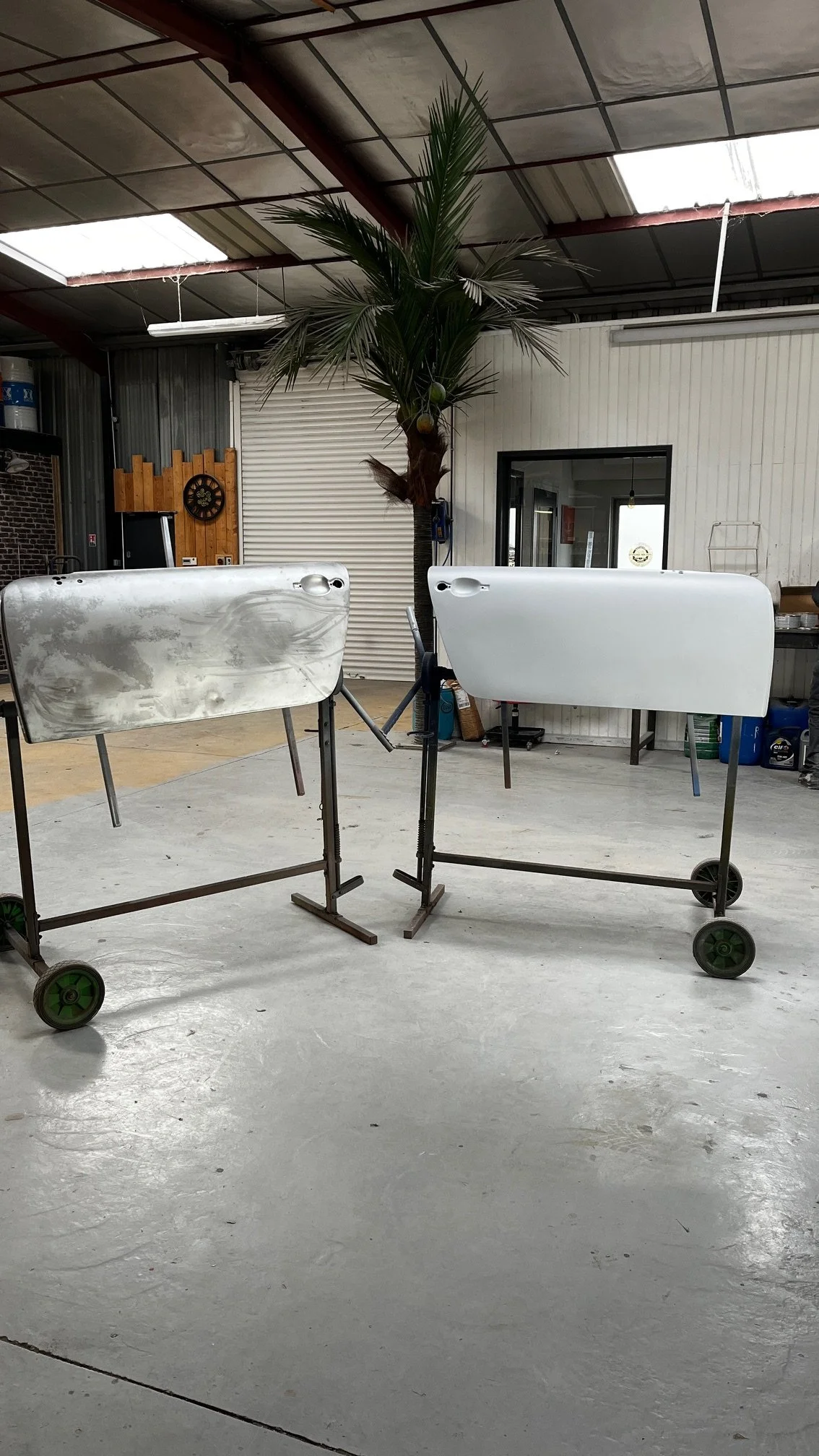 Deux portes de voiture sur des supports dans un atelier, avec une plante artificielle en arrière-plan.