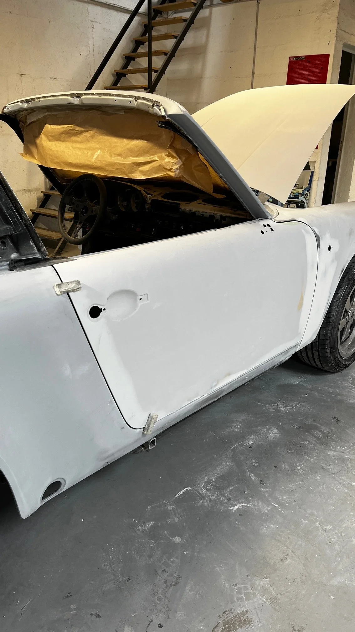 Voiture de course en cours de réparation ou de restauration dans un garage, sans porte et avec le capot levé.