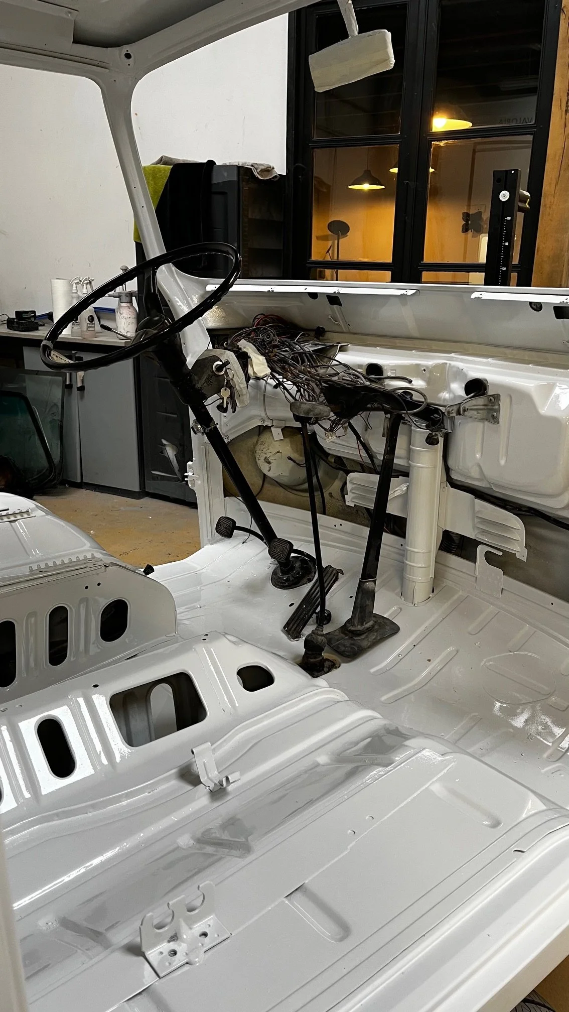 Intérieur d'une voiture en cours de restauration, dénuée de sièges, avec un tableau de bord en construction, dans un atelier.