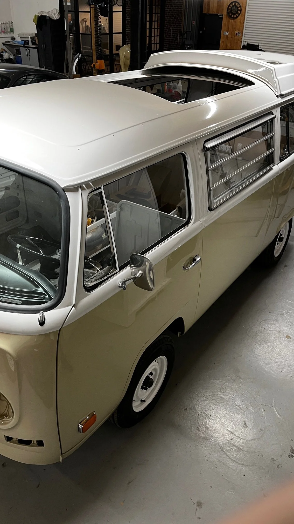 Voiture van vintage beige et blanche avec toit ouvrant, stationnée dans un garage