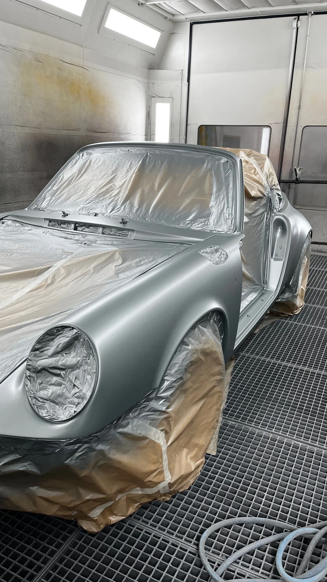 Voiture en cours de peinture dans un atelier, recouverte de papier protecteur et pulvérisée d'une couche de peinture argentée.