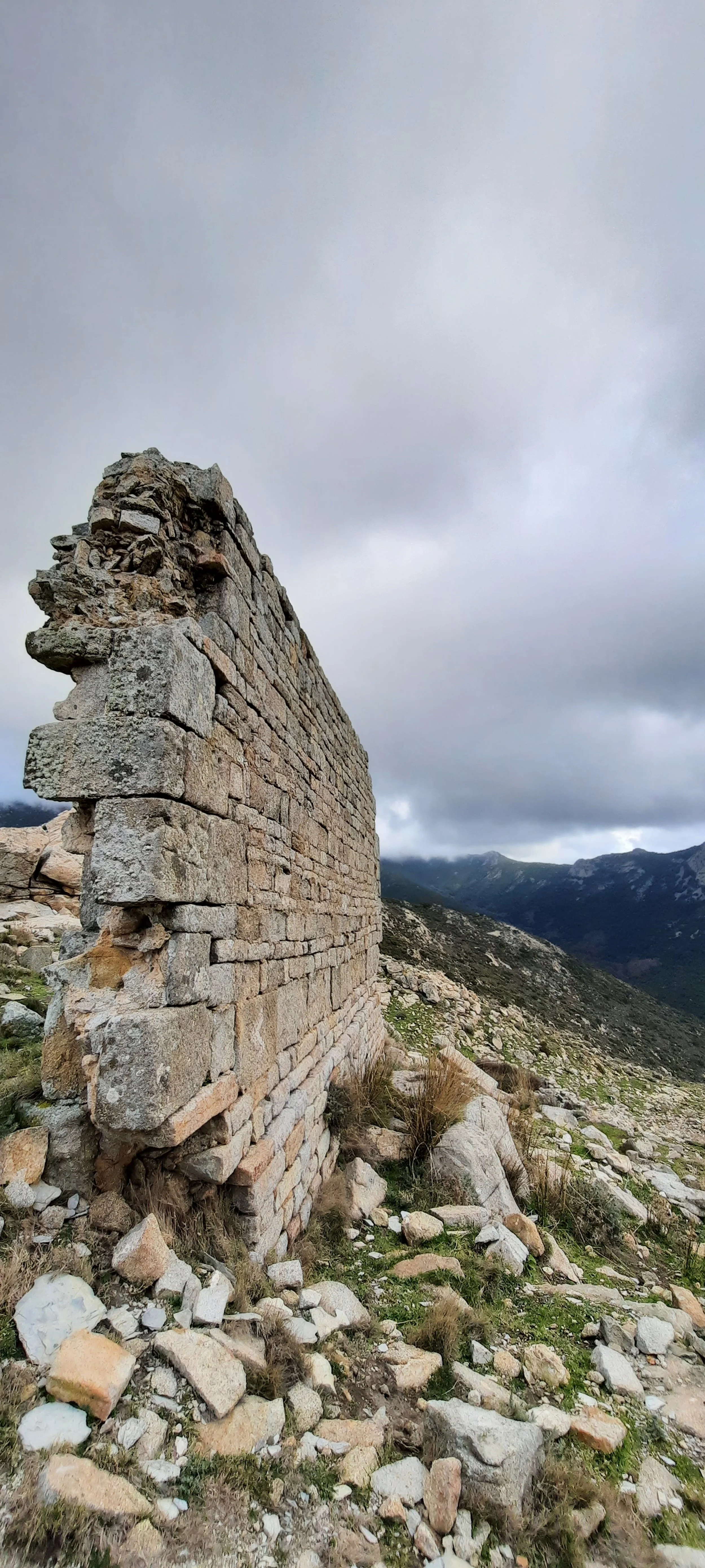 Particolare di un muro in pietra in montagna con sfondo di nuvole e montagne.